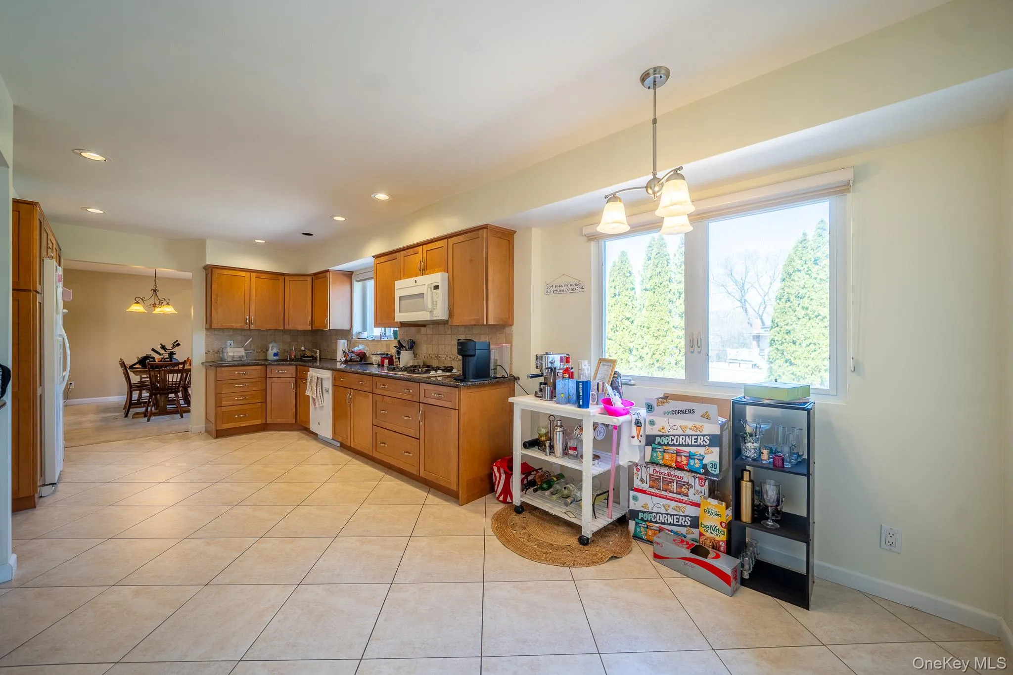 Kitchen with dark countertops, brown cabinets, decorative backsplash, white appliances, and an inviting chandelier Kitchen with dark countertops, brown cabinets, decorative backsplash, white appliances, and an inviting chandelier