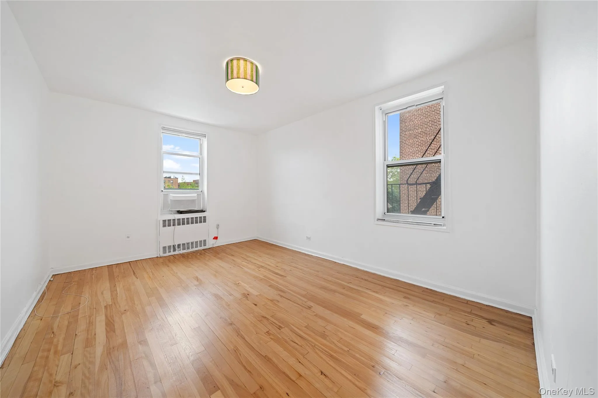 Hardwood flooring, painted walls, window-mounted air conditioning unit, and ceiling-mounted light fixture Hardwood flooring, painted walls, window-mounted air conditioning unit, and ceiling-mounted light fixture