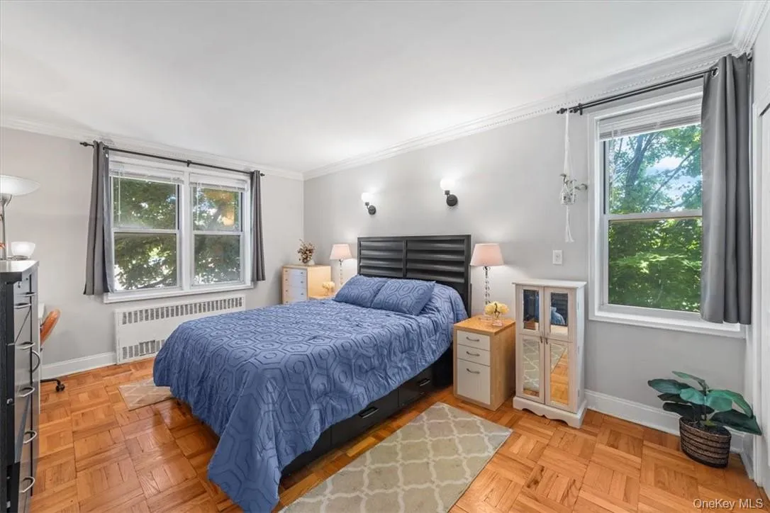 Bedroom featuring ornamental molding, radiator, and light parquet flooring Bedroom featuring ornamental molding, radiator, and light parquet flooring