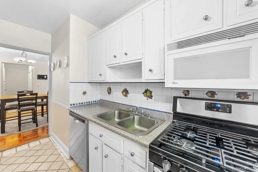 Kitchen with white cabinetry, tasteful backsplash, light parquet floors, appliances with stainless steel finishes, and sink Kitchen with white cabinetry, tasteful backsplash, light parquet floors, appliances with stainless steel finishes, and sink