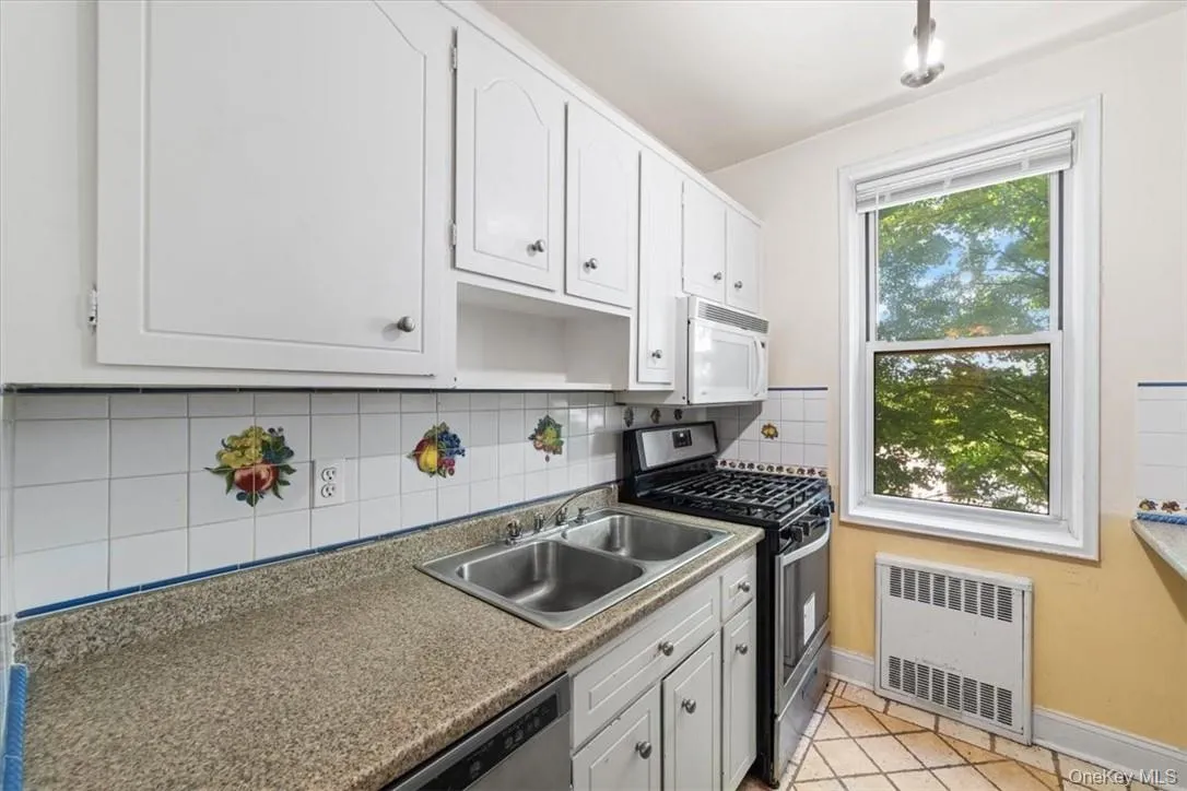 Kitchen with sink, stainless steel gas stove, light tile patterned flooring, radiator heating unit, and white cabinetry Kitchen with sink, stainless steel gas stove, light tile patterned flooring, radiator heating unit, and white cabinetry