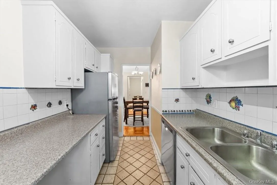 Kitchen with decorative backsplash, appliances with stainless steel finishes, light tile patterned floors, and white cabinets Kitchen with decorative backsplash, appliances with stainless steel finishes, light tile patterned floors, and white cabinets
