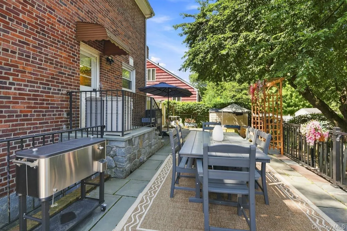 Brick exterior with stone foundation detailing, expansive patio with flagstone pavers, black wrought iron railing, and mature landscaping. Brick exterior with stone foundation detailing, expansive patio with flagstone pavers, black wrought iron railing, and mature landscaping.