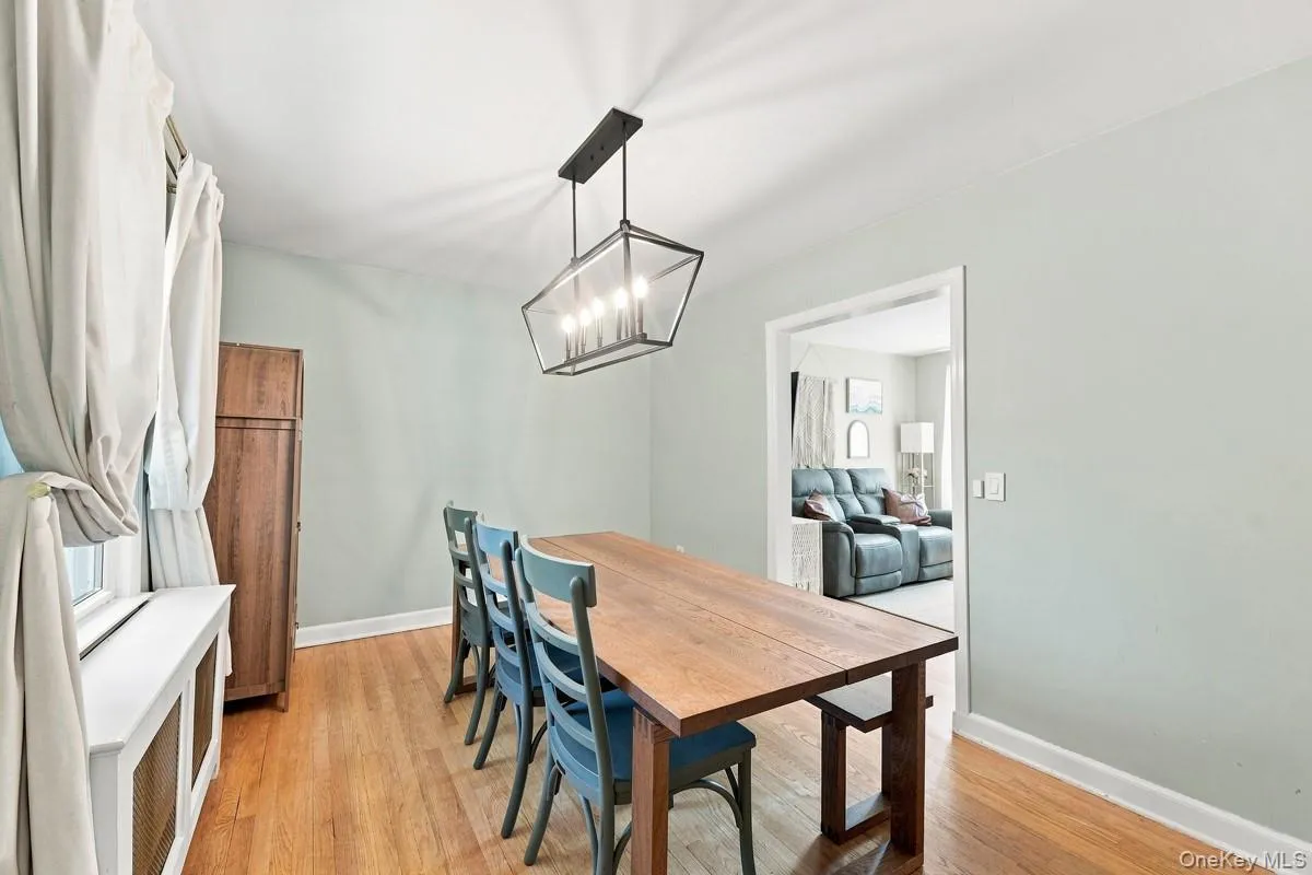 Dining room with hardwood flooring, doorway to living room, and a modern chandelier. Dining room with hardwood flooring, doorway to living room, and a modern chandelier.