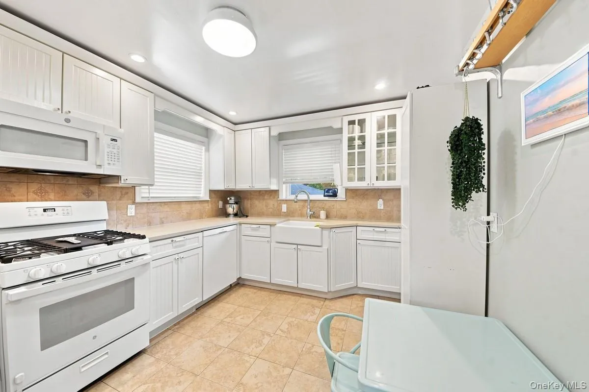 Kitchen featuring white cabinetry, ceramic tile flooring, spacious countertops, tile backsplash, and a farmhouse-style sink. Kitchen featuring white cabinetry, ceramic tile flooring, spacious countertops, tile backsplash, and a farmhouse-style sink.