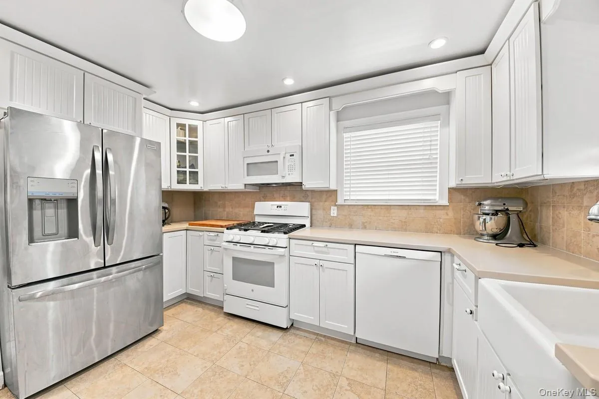 White cabinetry, stainless steel refrigerator, range, dishwasher, and a farmhouse sink. White cabinetry, stainless steel refrigerator, range, dishwasher, and a farmhouse sink.