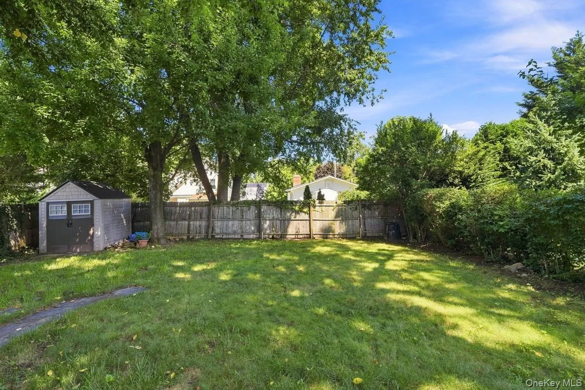 Expansive grassy yard with mature trees, a wood privacy fence, and a storage shed with double doors. Expansive grassy yard with mature trees, a wood privacy fence, and a storage shed with double doors.