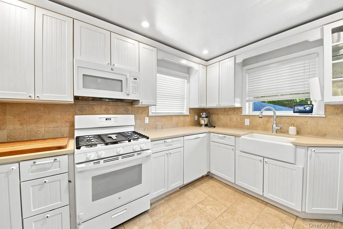 Kitchen featuring white cabinetry, ceramic tile flooring, light-toned countertops, and a farmhouse sink. Kitchen featuring white cabinetry, ceramic tile flooring, light-toned countertops, and a farmhouse sink.