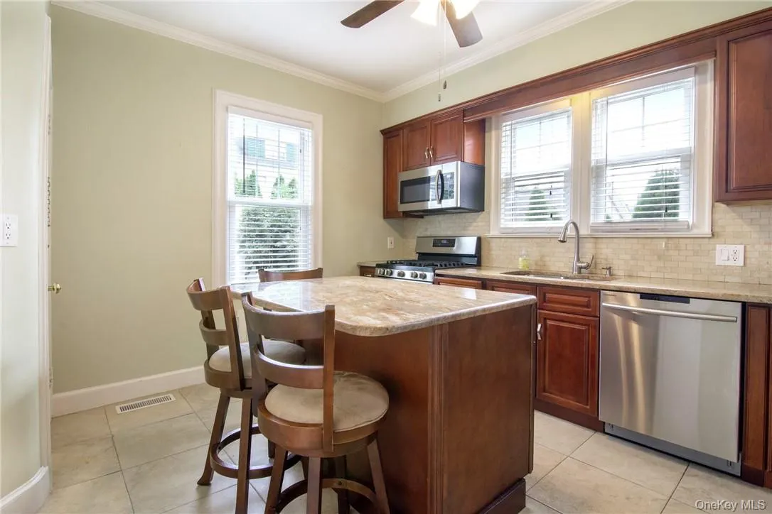 Kitchen with light stone counters, sink, ceiling fan, a kitchen island, and appliances with stainless steel finishes Kitchen with light stone counters, sink, ceiling fan, a kitchen island, and appliances with stainless steel finishes