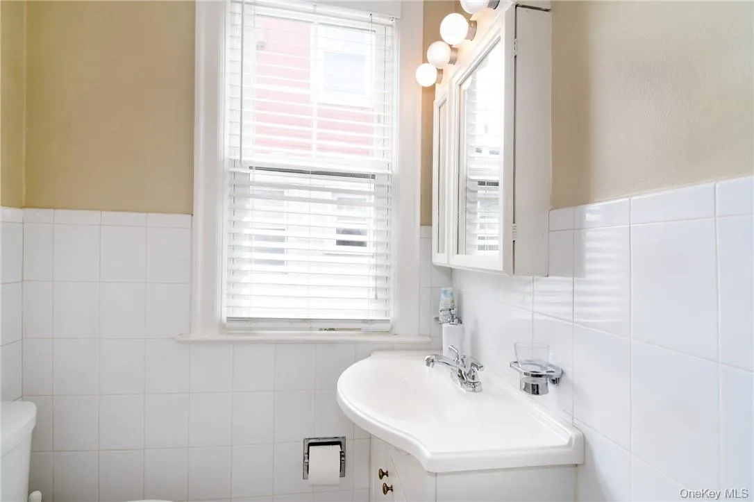 Bathroom featuring tile walls, toilet, a wealth of natural light, and vanity Bathroom featuring tile walls, toilet, a wealth of natural light, and vanity