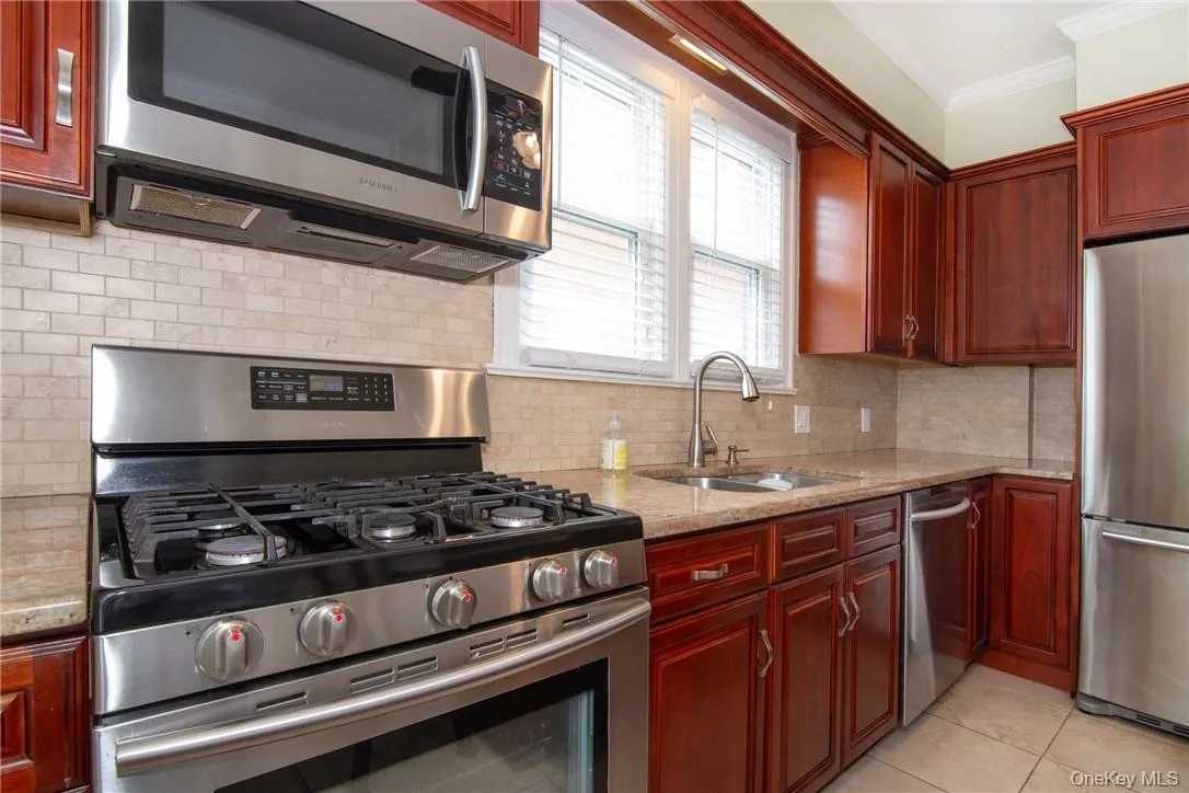 Kitchen featuring light stone countertops, crown molding, stainless steel appliances, sink, and light tile patterned flooring Kitchen featuring light stone countertops, crown molding, stainless steel appliances, sink, and light tile patterned flooring