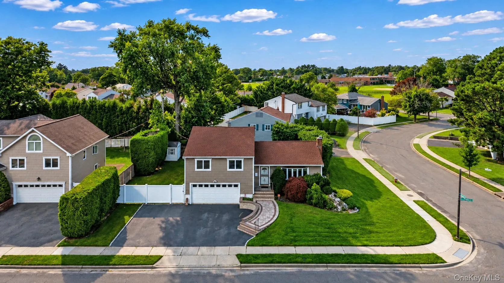 Corner property Split-level residence featuring a two-car garage, established landscaping, and a curvilinear paved driveway Corner property Split-level residence featuring a two-car garage, established landscaping, and a curvilinear paved driveway