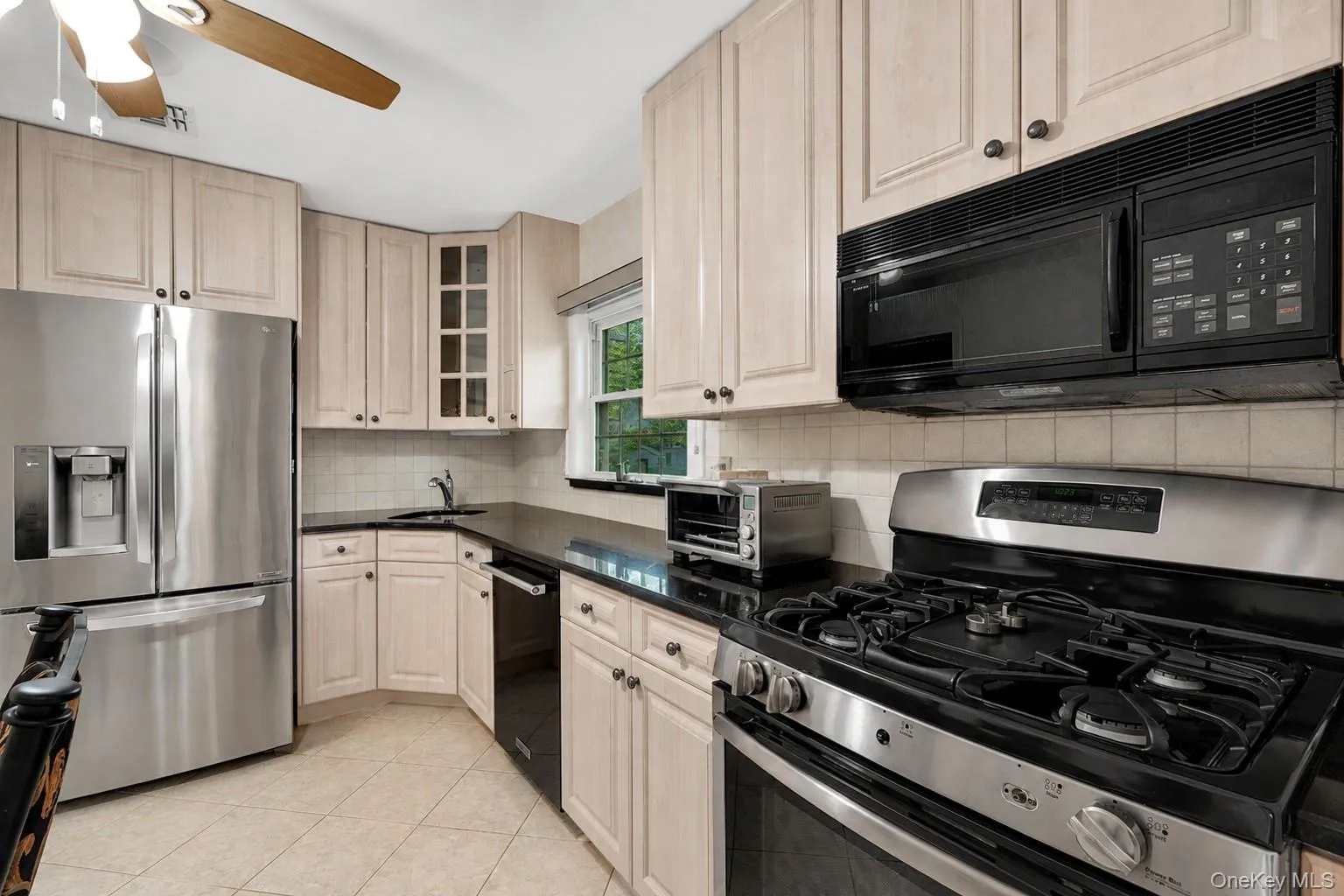 Kitchen featuring light wood-finish cabinetry, dark countertops, and stainless steel appliances Kitchen featuring light wood-finish cabinetry, dark countertops, and stainless steel appliances