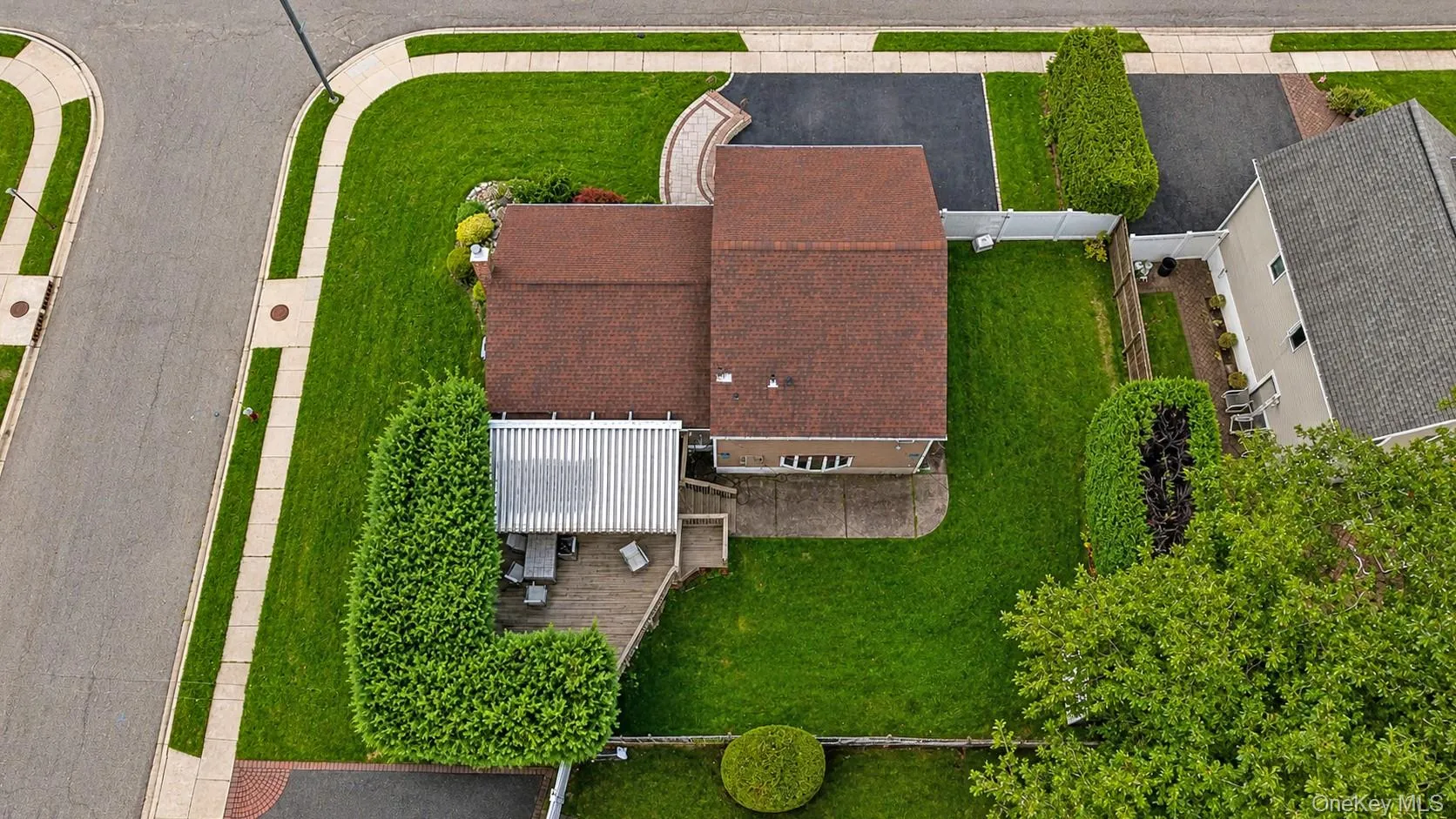 Exterior featuring a brown shingled roof, a paved patio with a pergola, extensive green lawn, and mature perimeter hedging Exterior featuring a brown shingled roof, a paved patio with a pergola, extensive green lawn, and mature perimeter hedging