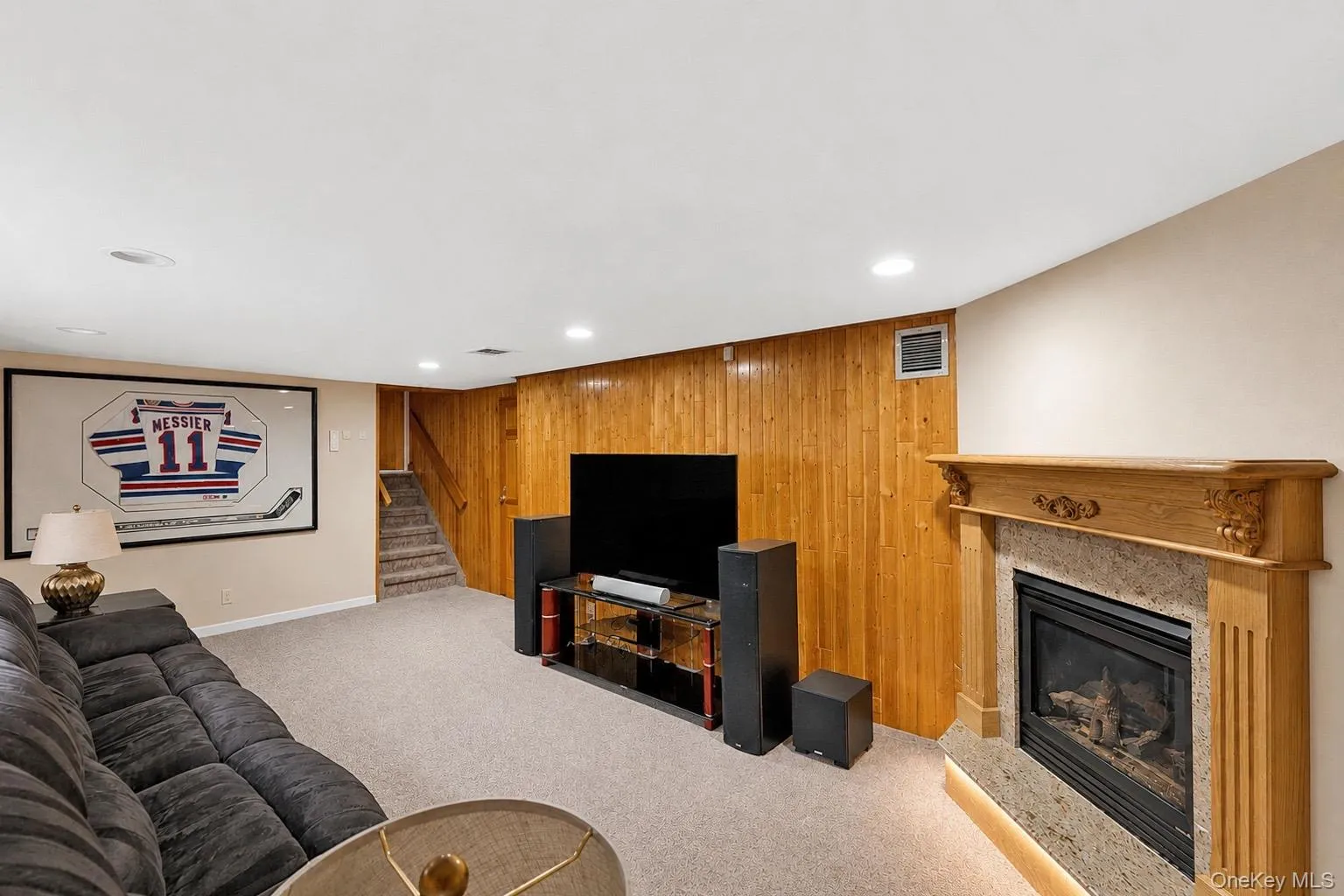 Carpeted living space featuring a wood-paneled accent wall and a built-in fireplace with a stone surround and wood mantel Carpeted living space featuring a wood-paneled accent wall and a built-in fireplace with a stone surround and wood mantel