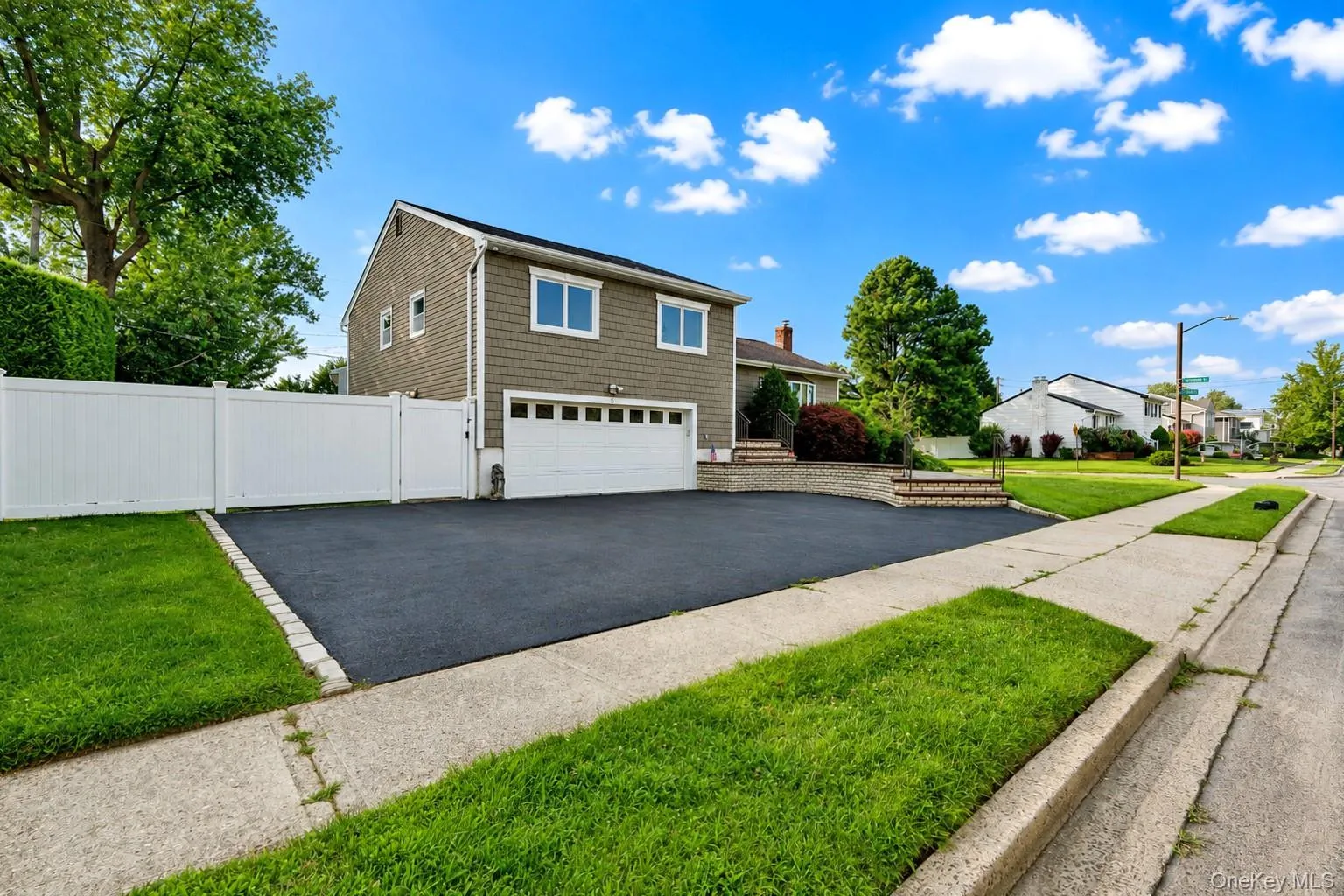 Shingle-sided residence featuring a two-car garage, white vinyl fencing, and a blacktop driveway Shingle-sided residence featuring a two-car garage, white vinyl fencing, and a blacktop driveway
