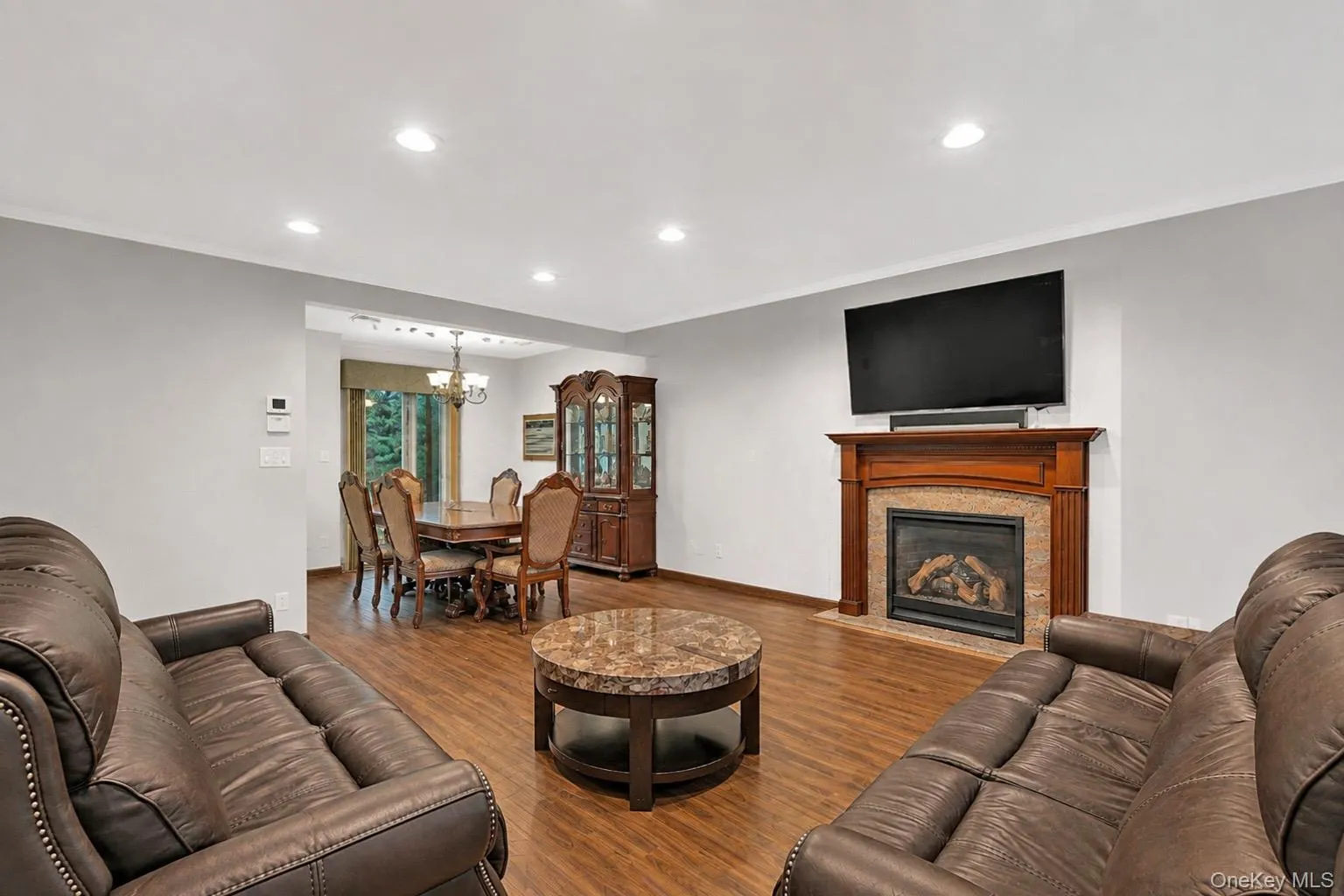 Living area with wood-finish flooring, recessed lighting, and a fireplace featuring a wood mantel and tile surround Living area with wood-finish flooring, recessed lighting, and a fireplace featuring a wood mantel and tile surround