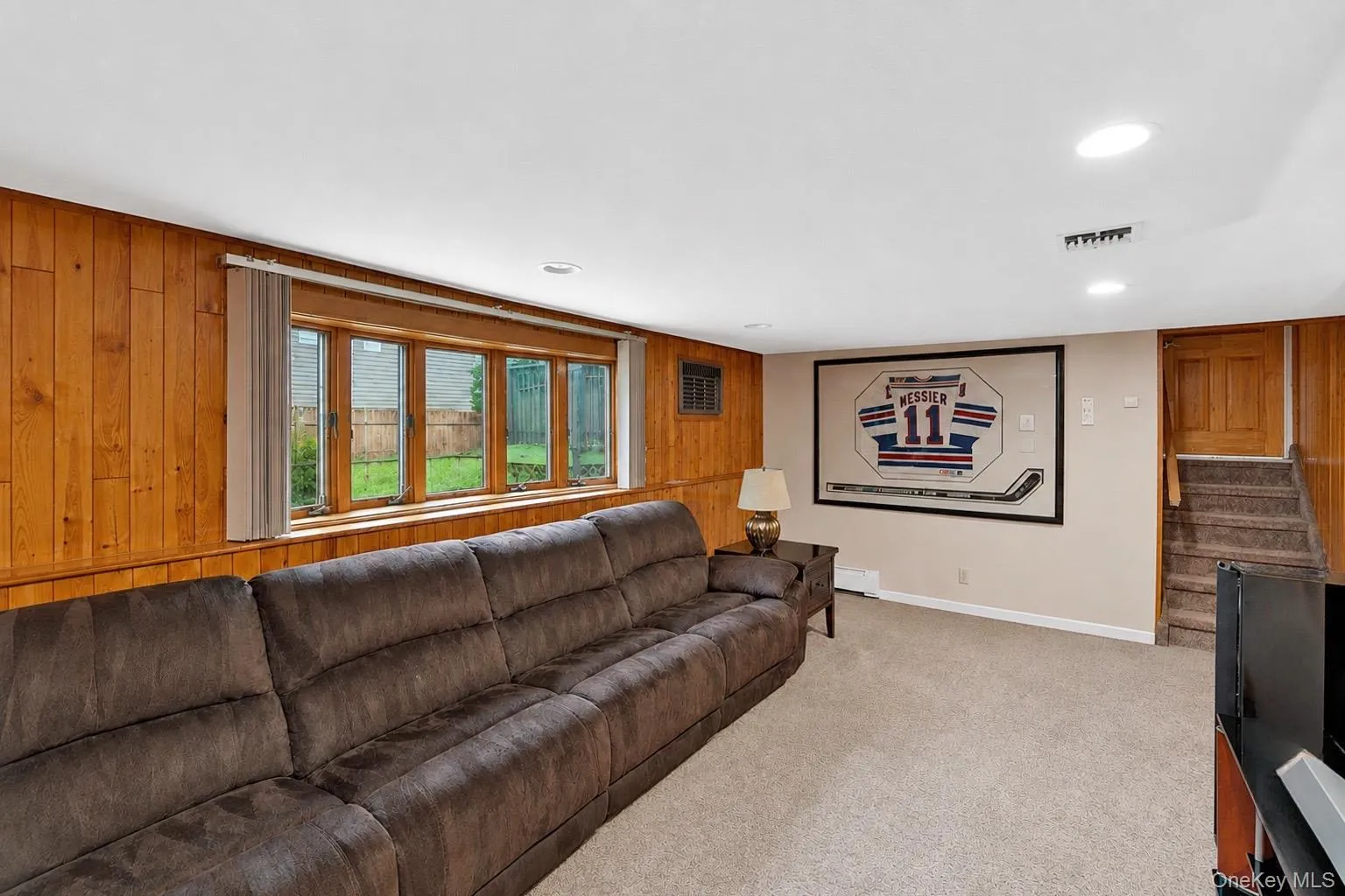 Recessed lighting illuminates this carpeted room, featuring wood paneling along one wall Recessed lighting illuminates this carpeted room, featuring wood paneling along one wall