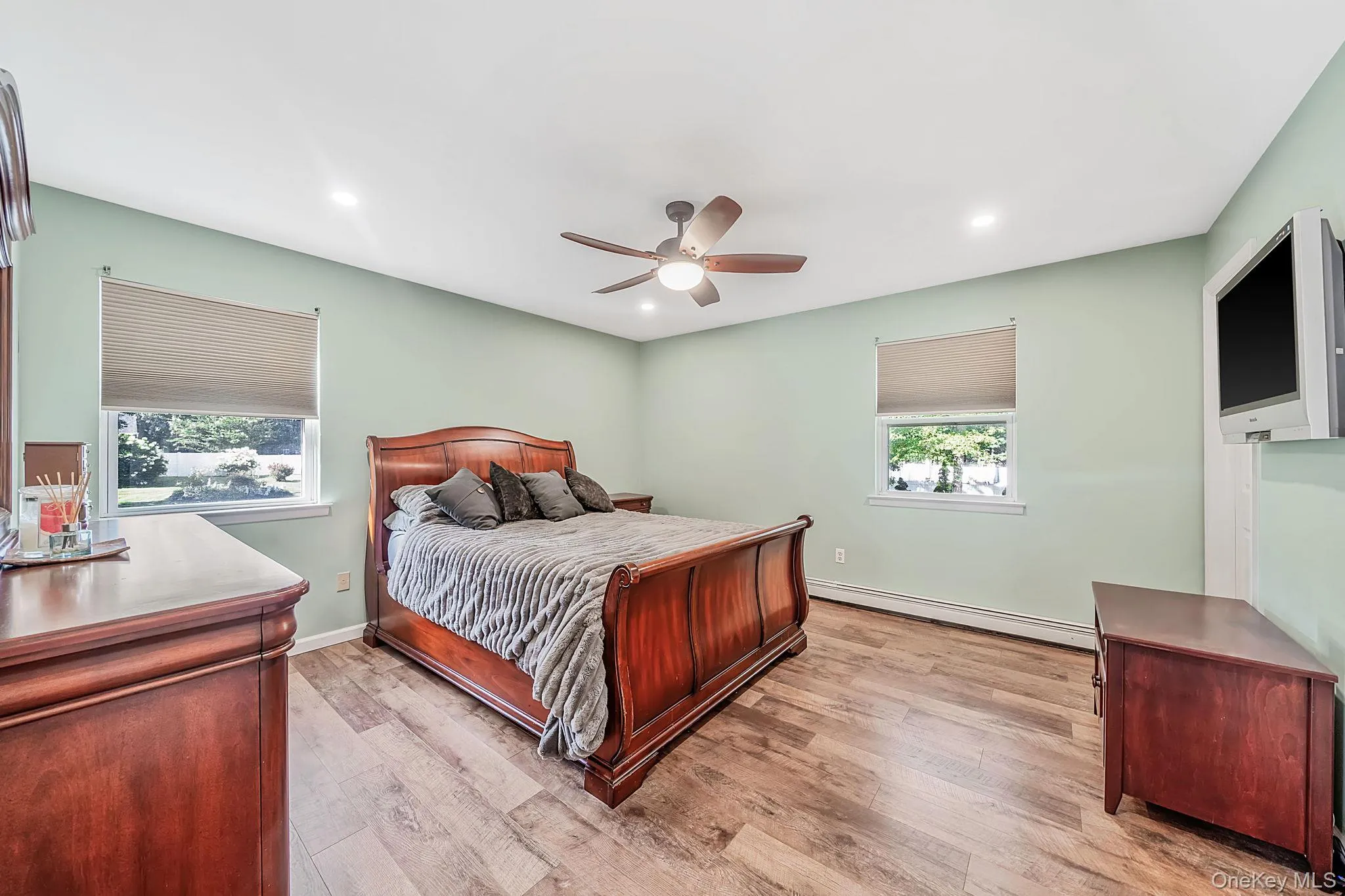 Spacious room featuring wood-finish flooring, two windows with window treatments, a ceiling fan, and recessed lighting Spacious room featuring wood-finish flooring, two windows with window treatments, a ceiling fan, and recessed lighting
