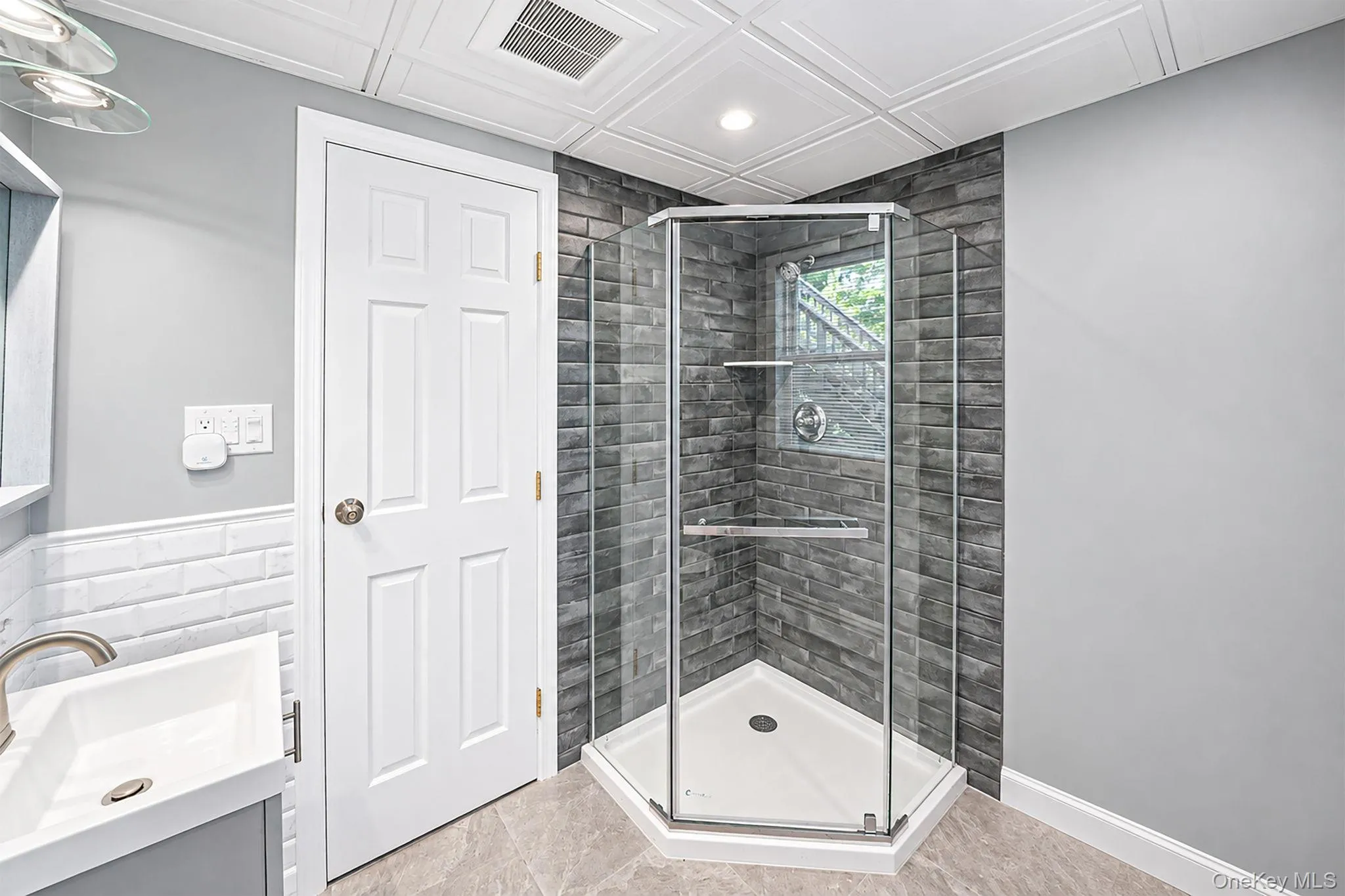 Corner glass-enclosed shower with dark stacked stone-look tile surround and built-in shelving Corner glass-enclosed shower with dark stacked stone-look tile surround and built-in shelving