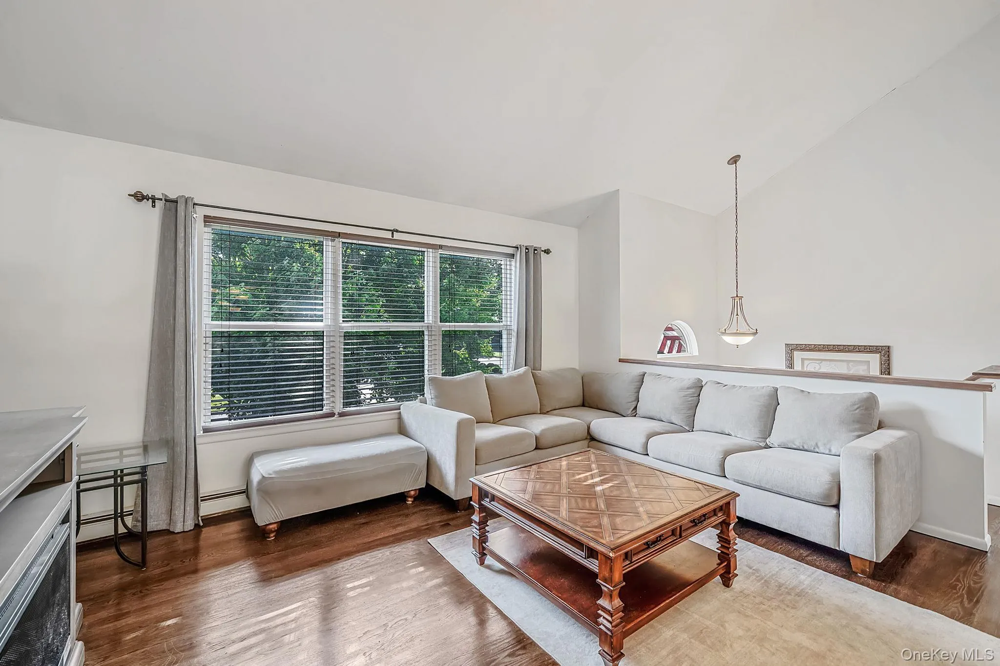 Living area with hardwood flooring, a large window, a partial wall, and a sloped ceiling Living area with hardwood flooring, a large window, a partial wall, and a sloped ceiling