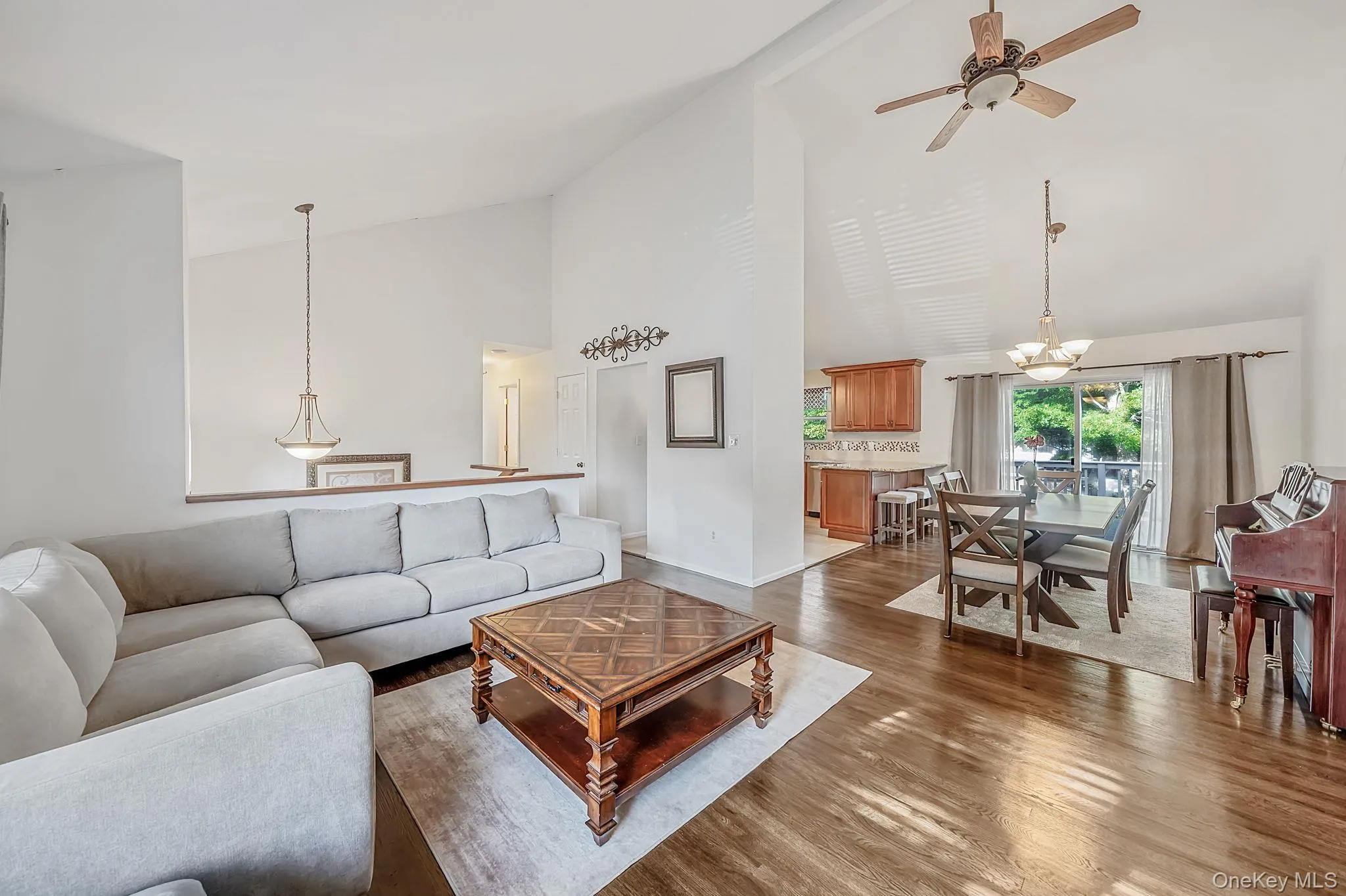 Spacious living area featuring vaulted ceilings, wood-finish flooring, and natural light Spacious living area featuring vaulted ceilings, wood-finish flooring, and natural light