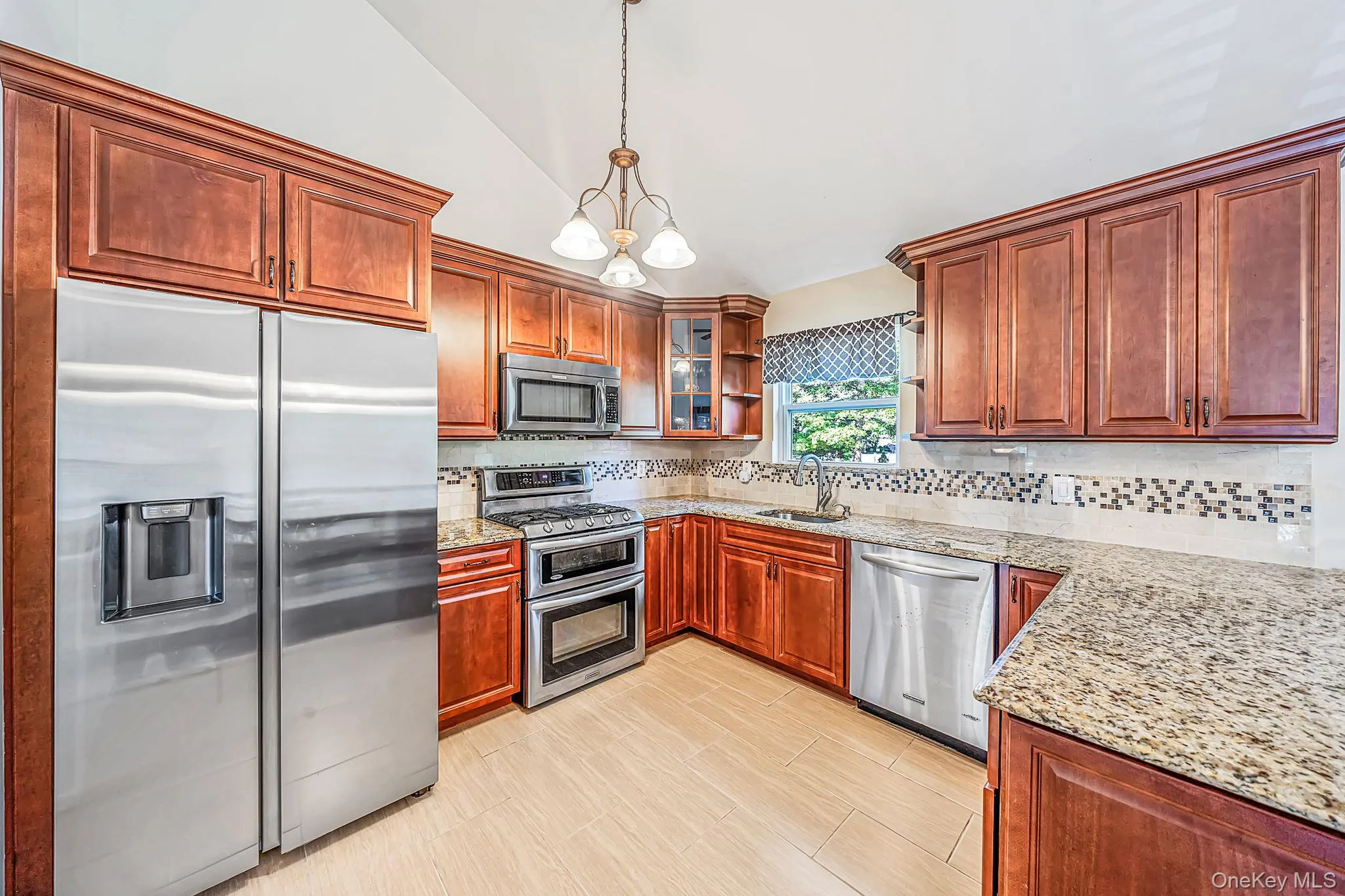 Chef's kitchen featuring rich wood cabinetry, stainless steel appliances including dual wall ovens and side-by-side refrigerator, granite countertops, decorative tile backsplash, pendant lighting, and light wood-finish flooring throughout Chef's kitchen featuring rich wood cabinetry, stainless steel appliances including dual wall ovens and side-by-side refrigerator, granite countertops, decorative tile backsplash, pendant lighting, and light wood-finish flooring throughout