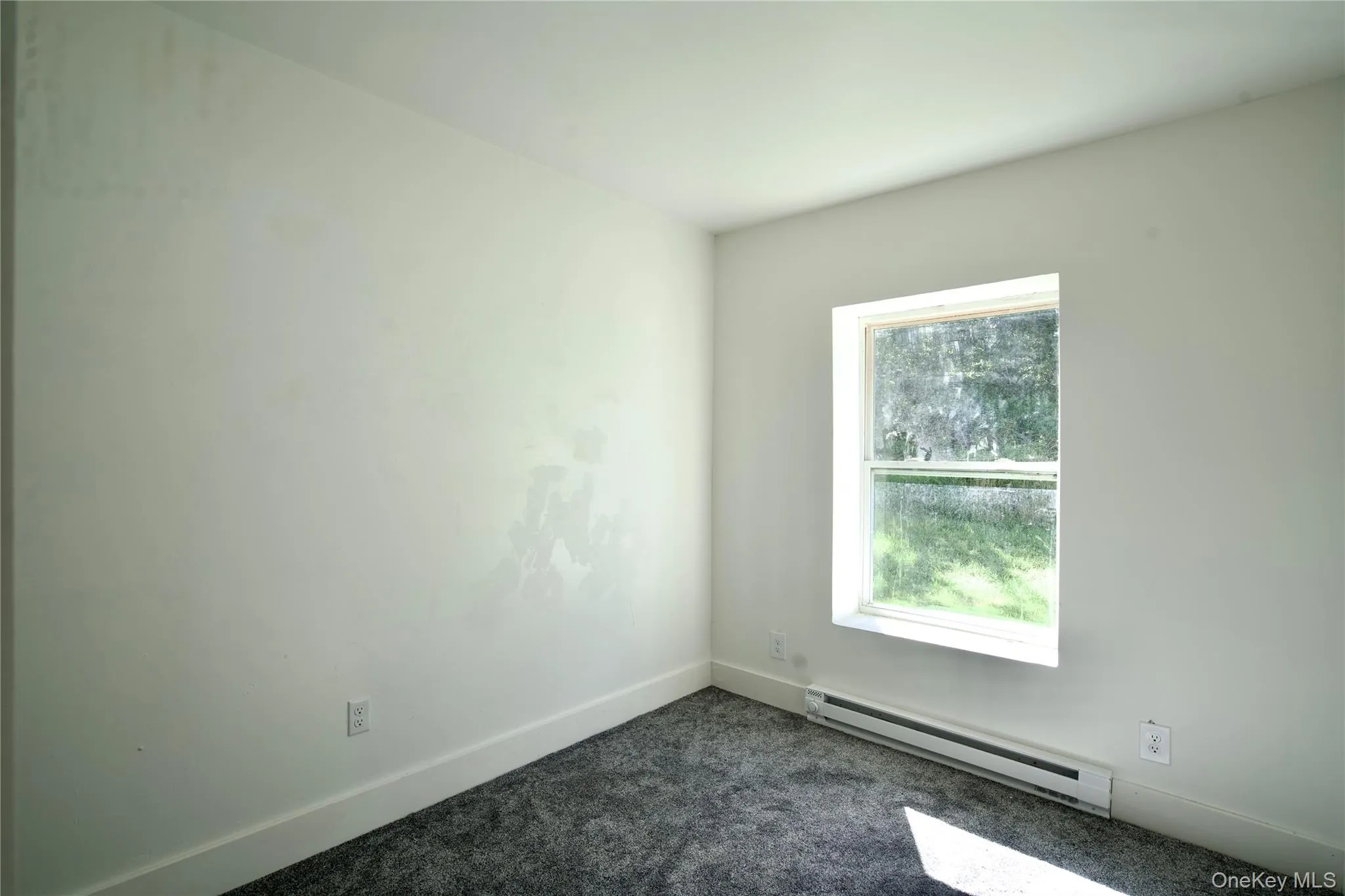 Empty room with baseboard heating and dark colored carpet Empty room with baseboard heating and dark colored carpet