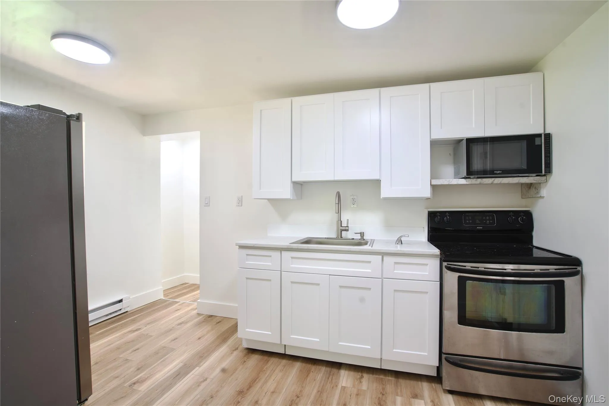 Kitchen featuring appliances with stainless steel finishes, white cabinetry, light countertops, light wood finished floors, and a baseboard heating unit Kitchen featuring appliances with stainless steel finishes, white cabinetry, light countertops, light wood finished floors, and a baseboard heating unit