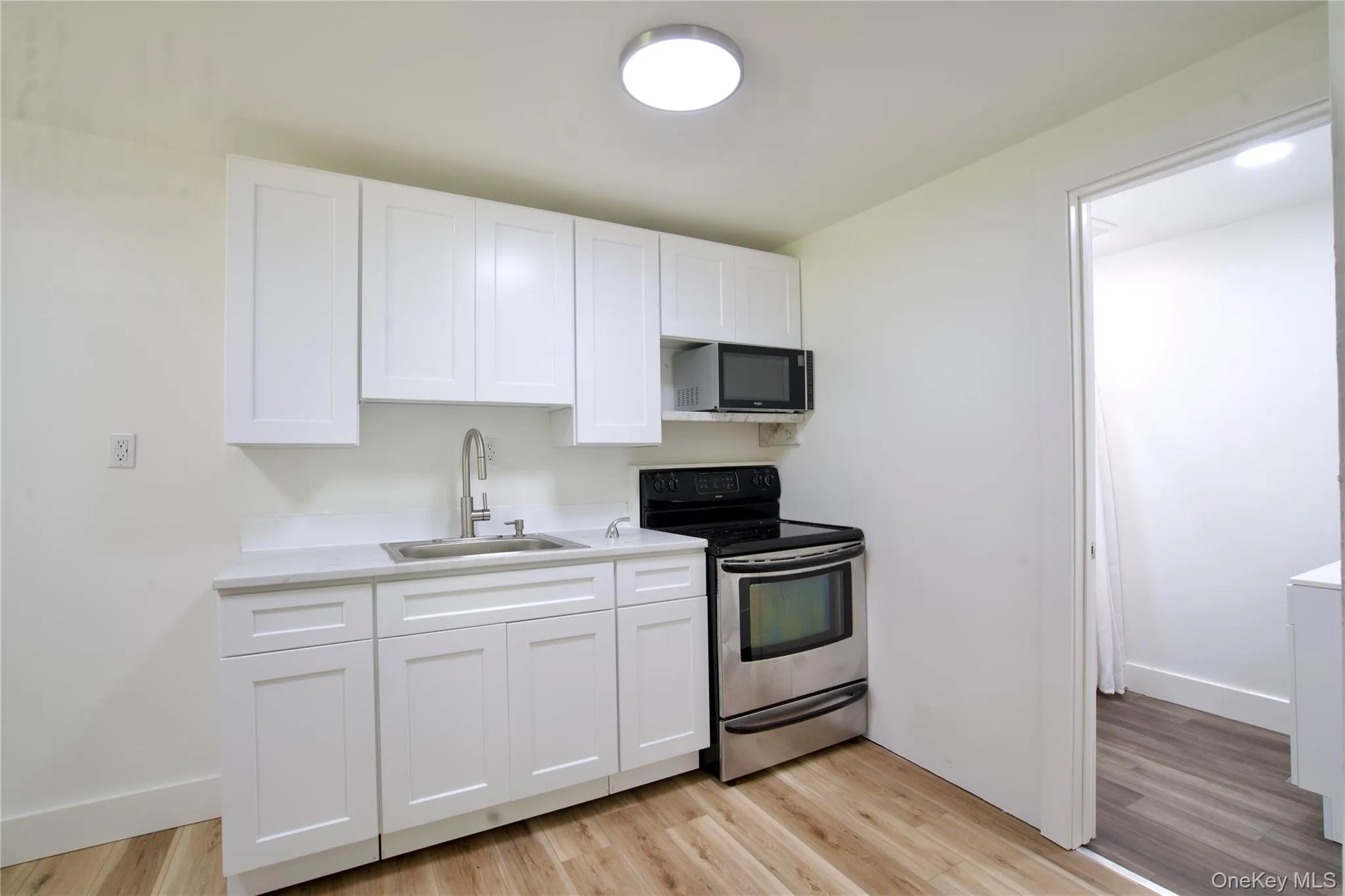 Kitchen with stainless steel range with electric stovetop, white cabinets, black microwave, light countertops, and light wood-style flooring Kitchen with stainless steel range with electric stovetop, white cabinets, black microwave, light countertops, and light wood-style flooring