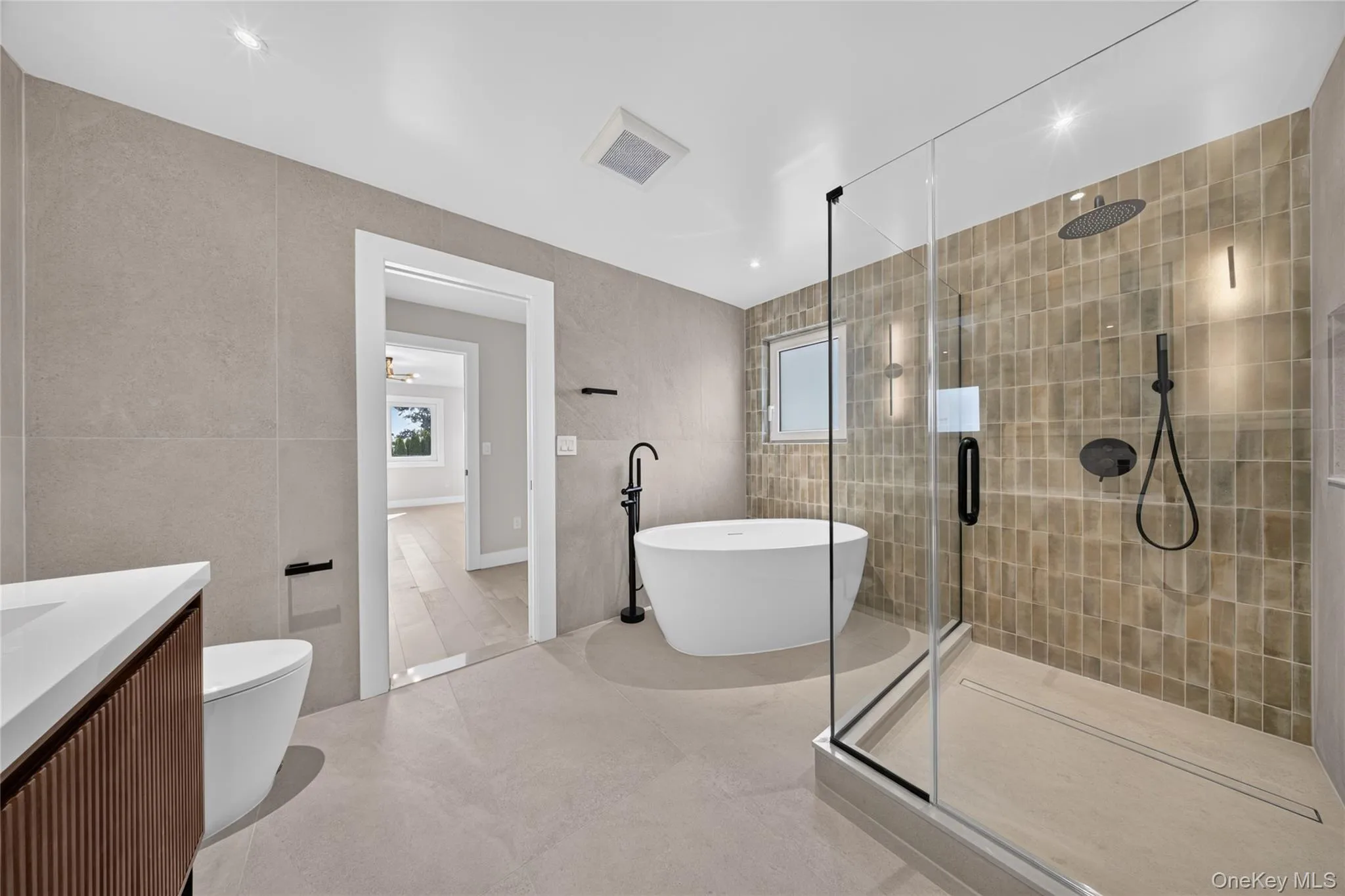 Freestanding soaking tub, glass-enclosed shower, wall-mounted showerhead, and matte black fixtures Freestanding soaking tub, glass-enclosed shower, wall-mounted showerhead, and matte black fixtures