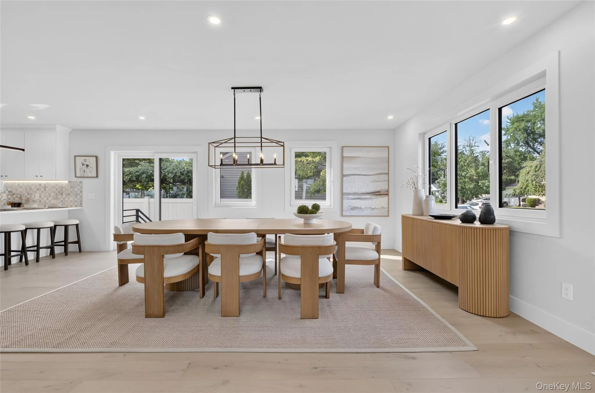 Recessed lighting, wood-finish flooring, a contemporary linear chandelier, multiple large windows, and white walls Recessed lighting, wood-finish flooring, a contemporary linear chandelier, multiple large windows, and white walls