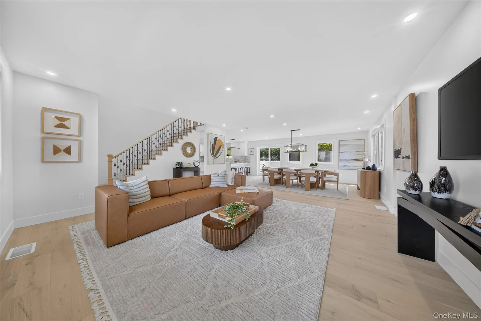 Open-concept interior featuring wood-finish flooring, recessed lighting, a staircase with decorative balusters, and multiple windows Open-concept interior featuring wood-finish flooring, recessed lighting, a staircase with decorative balusters, and multiple windows