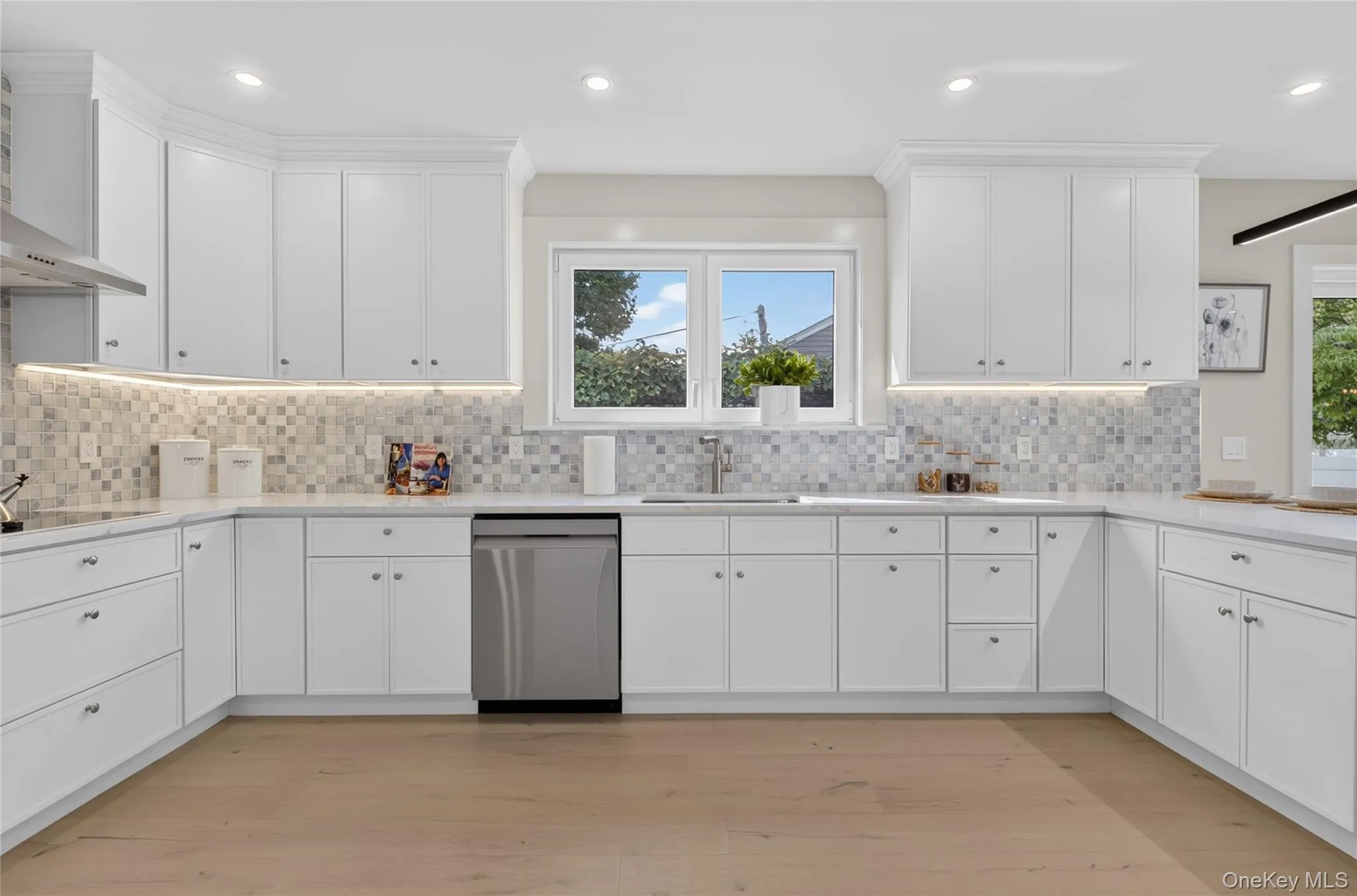 Kitchen featuring white shaker cabinetry, stainless steel appliances, mosaic tile backsplash, light wood-finish flooring, and recessed lighting Kitchen featuring white shaker cabinetry, stainless steel appliances, mosaic tile backsplash, light wood-finish flooring, and recessed lighting