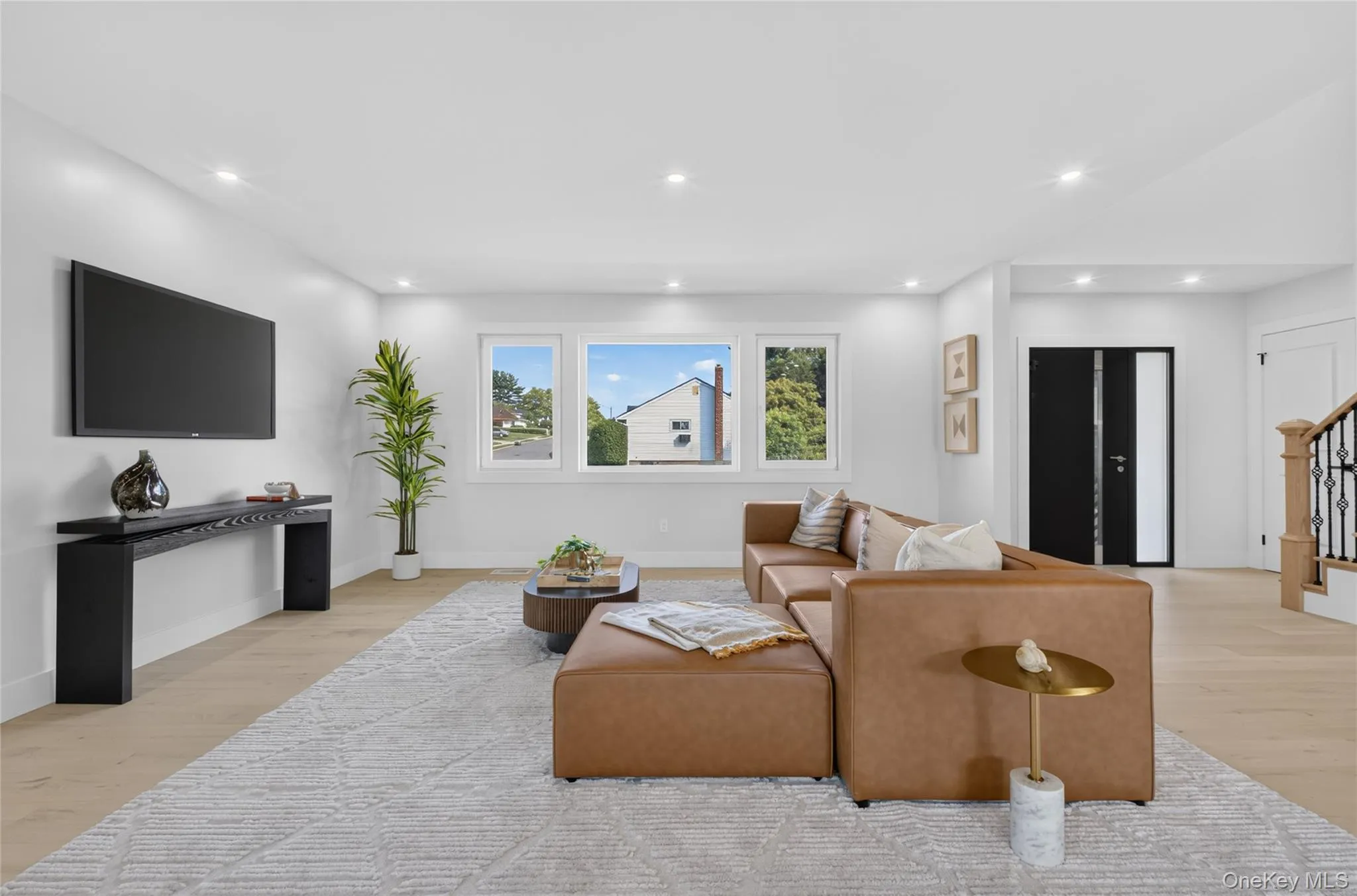 Recessed lighting, light wood-finish flooring, multiple windows, a modern entryway door, and a staircase with an iron baluster Recessed lighting, light wood-finish flooring, multiple windows, a modern entryway door, and a staircase with an iron baluster