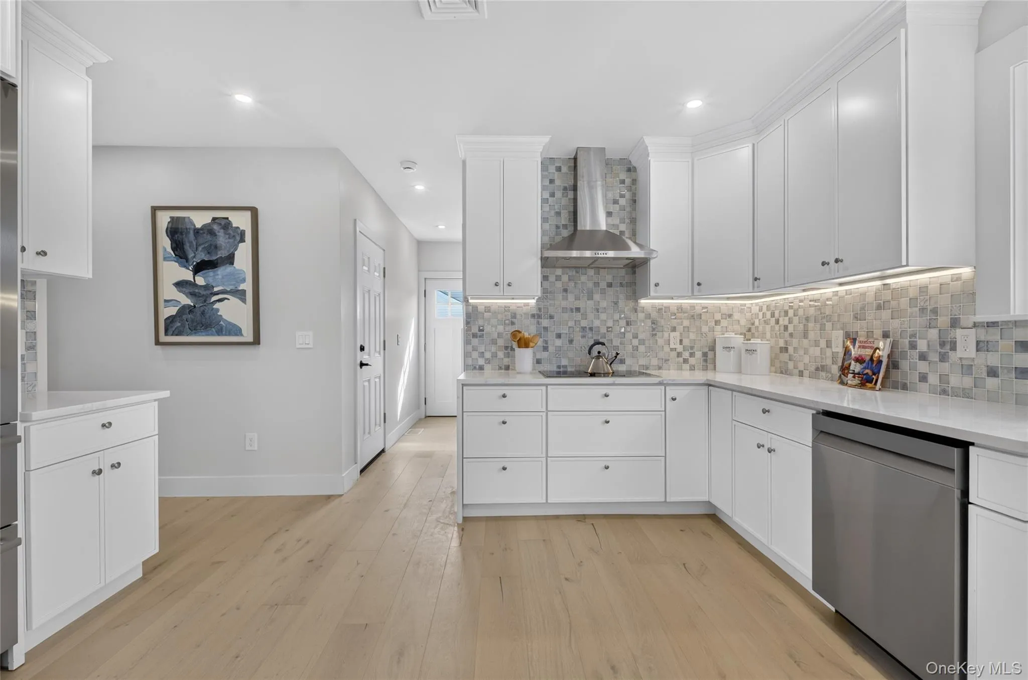 Kitchen featuring white shaker cabinetry, light wood-finish flooring, recessed lighting, and stainless steel appliances Kitchen featuring white shaker cabinetry, light wood-finish flooring, recessed lighting, and stainless steel appliances