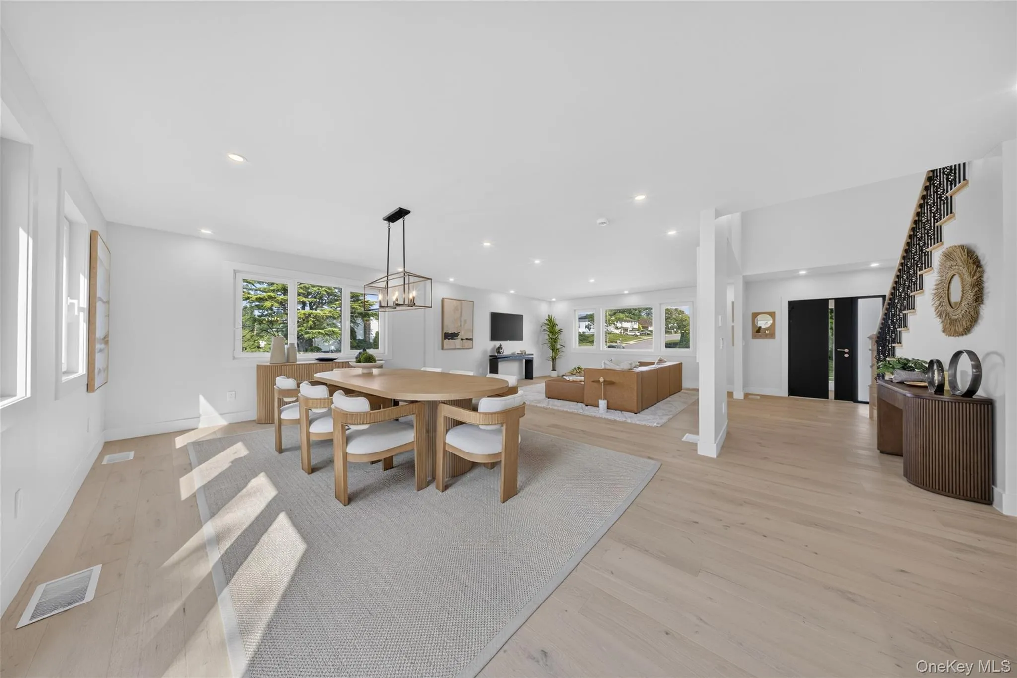 Expansive open-concept living space with light wood-finish flooring, recessed lighting, and large windows Expansive open-concept living space with light wood-finish flooring, recessed lighting, and large windows