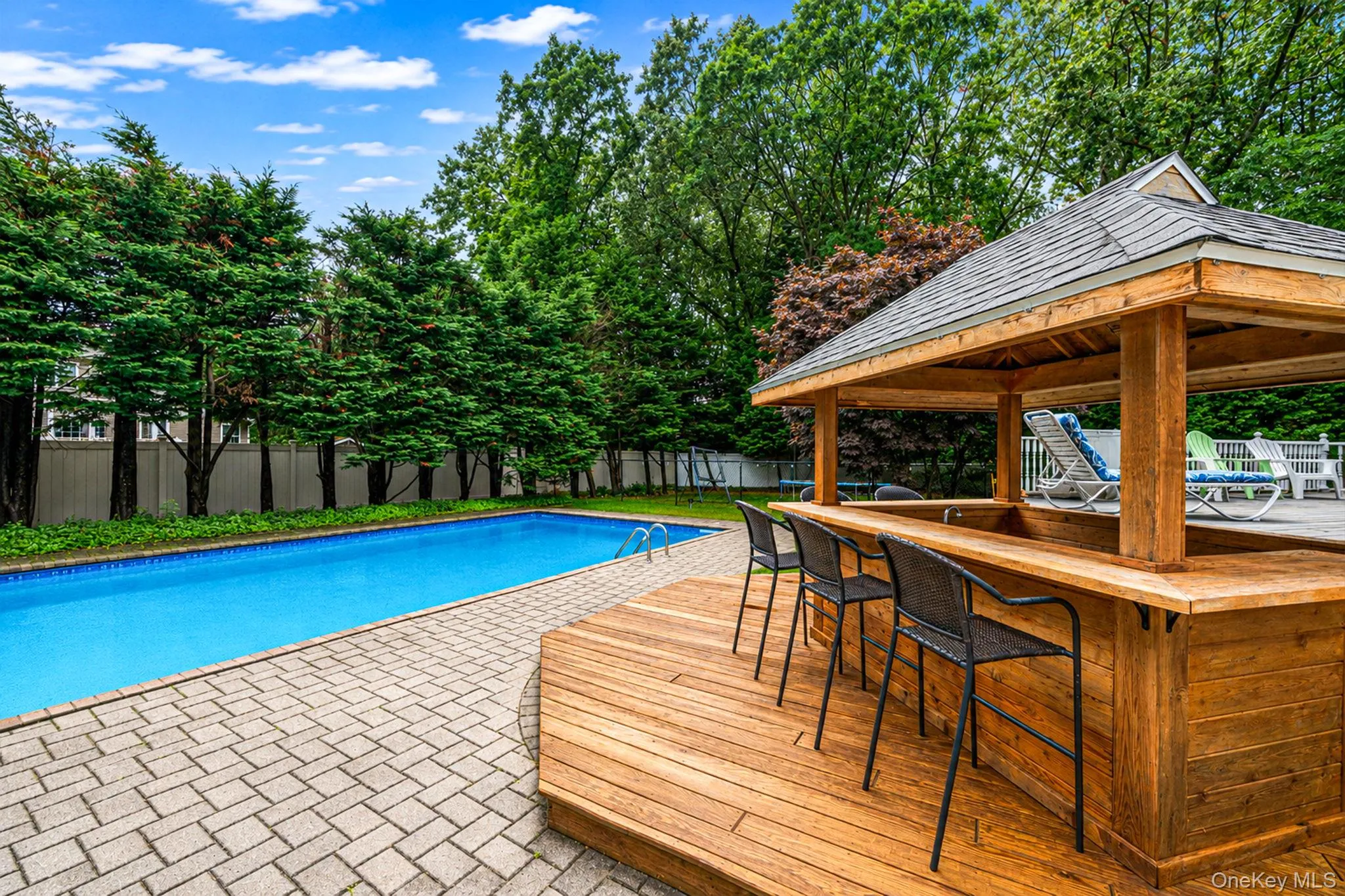 Outdoor entertainment area featuring a rectangular pool with paver surround, a built-in tiki bar electrified with water hookup, and a wood deck Outdoor entertainment area featuring a rectangular pool with paver surround, a built-in tiki bar electrified with water hookup, and a wood deck