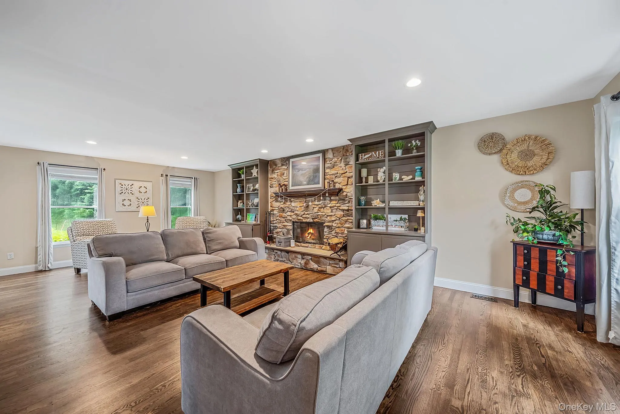Spacious living area featuring rich hardwood flooring, a stone-clad fireplace, and built-in shelving Spacious living area featuring rich hardwood flooring, a stone-clad fireplace, and built-in shelving