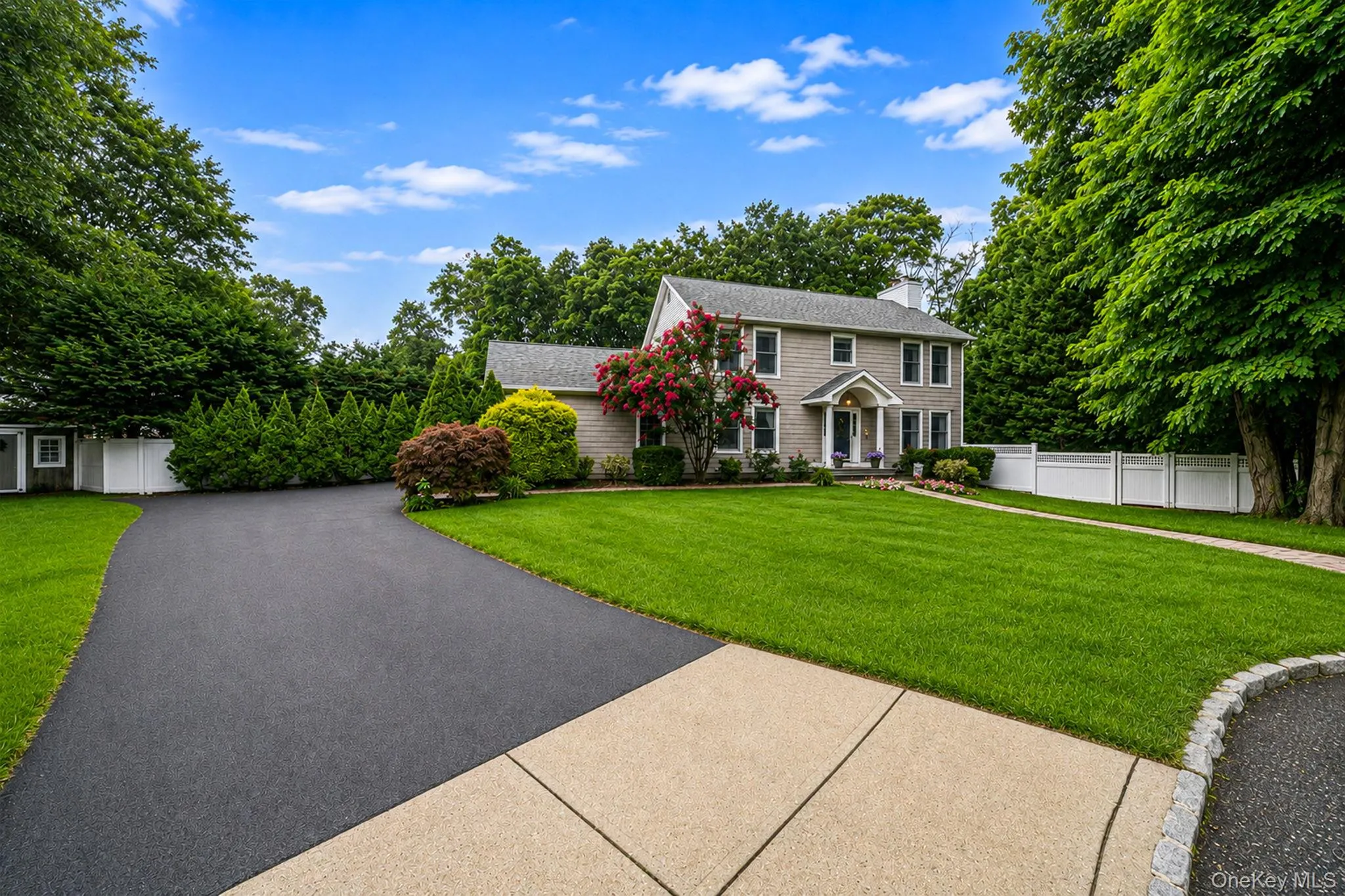Traditional-style residence featuring a prominent front lawn, mature trees, and a paved driveway Traditional-style residence featuring a prominent front lawn, mature trees, and a paved driveway