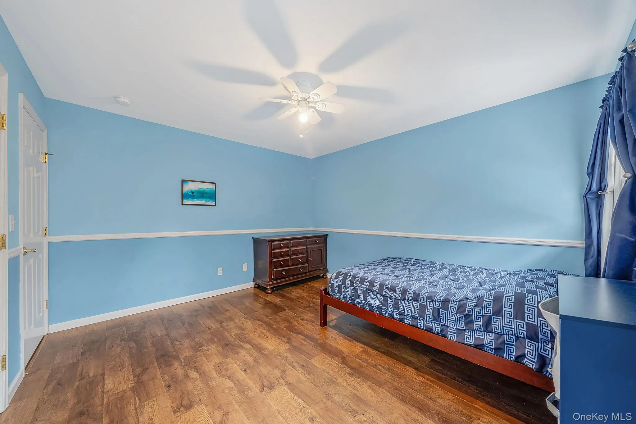Room featuring wood-finish flooring, white chair rail, and a ceiling fan with integrated lighting Room featuring wood-finish flooring, white chair rail, and a ceiling fan with integrated lighting