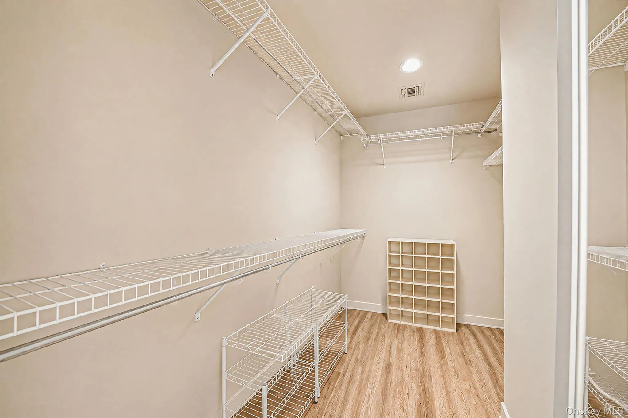 Walk-in closet featuring extensive wire shelving, hanging rods, wood-finish flooring, and recessed lighting Walk-in closet featuring extensive wire shelving, hanging rods, wood-finish flooring, and recessed lighting