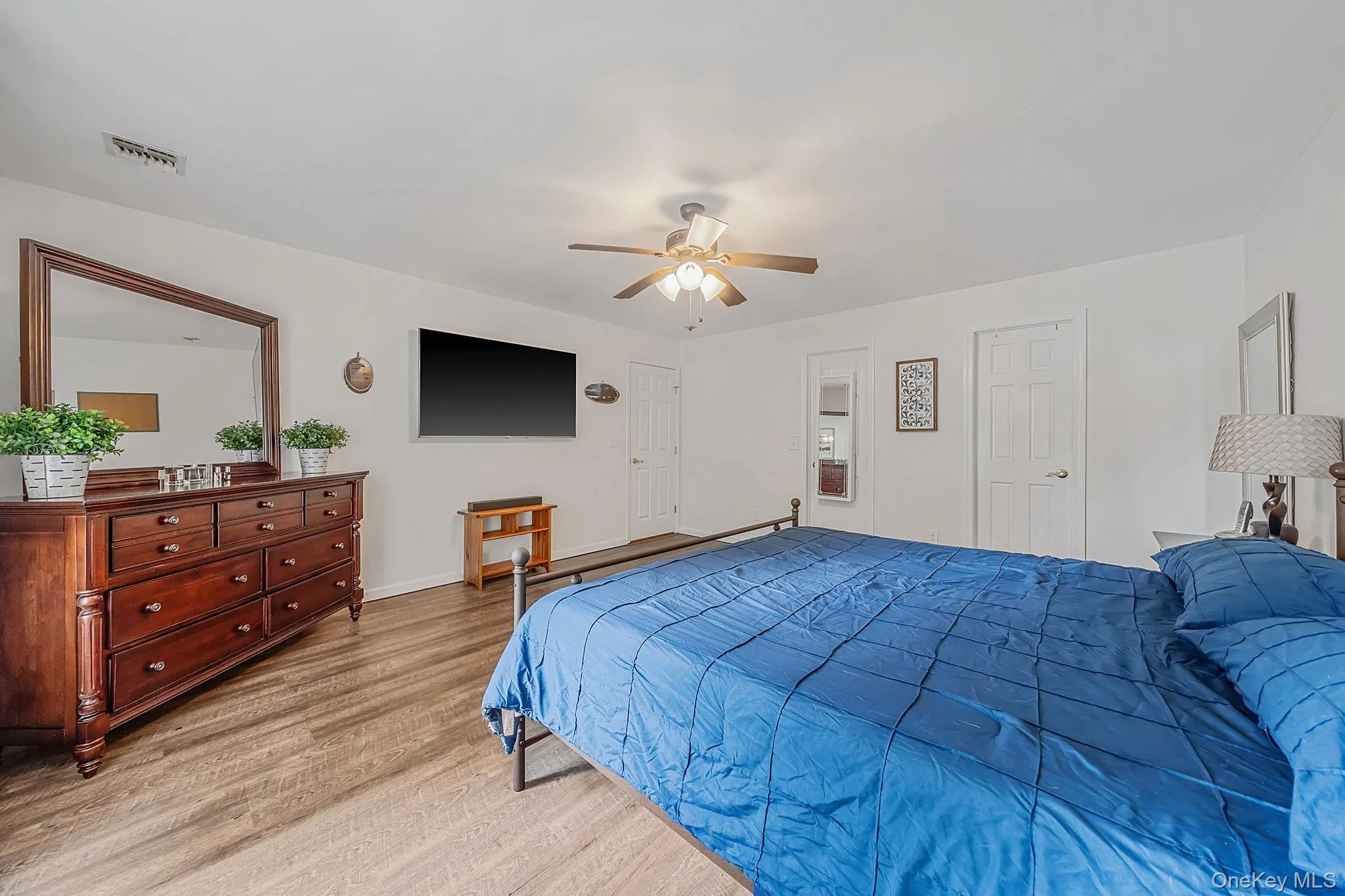 Spacious room featuring wood-finish flooring, a ceiling fan with integrated lighting, and white paneled doors Spacious room featuring wood-finish flooring, a ceiling fan with integrated lighting, and white paneled doors