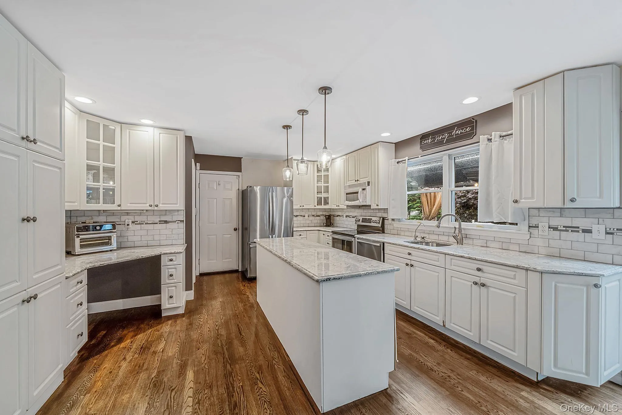 Kitchen featuring white cabinetry, light countertops, subway tile backsplash, hardwood flooring, and a central island Kitchen featuring white cabinetry, light countertops, subway tile backsplash, hardwood flooring, and a central island