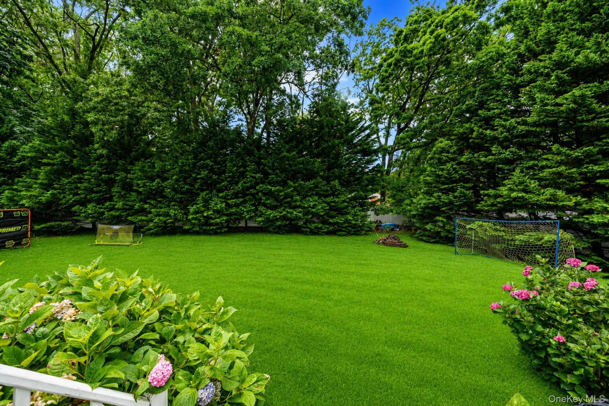 Expansive green lawn surrounded by mature trees and shrubs, featuring a white railing in the foreground Expansive green lawn surrounded by mature trees and shrubs, featuring a white railing in the foreground