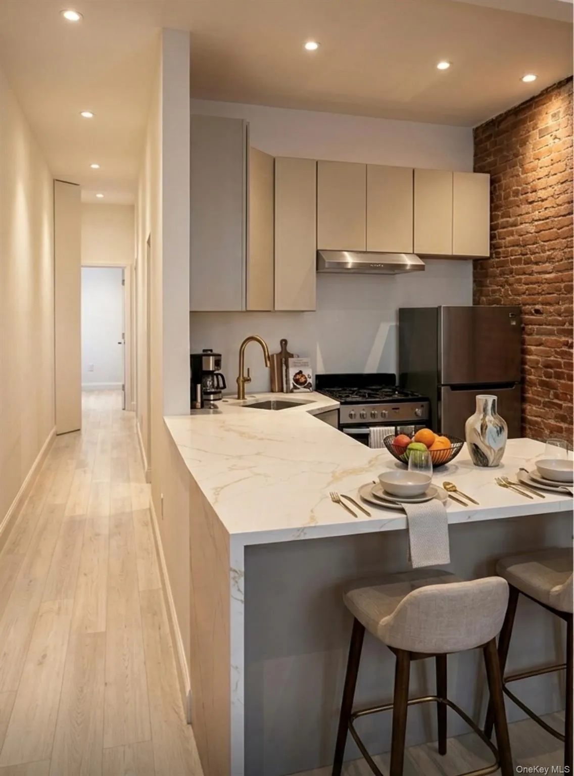 Modern kitchen featuring a waterfall-edge countertop, stainless steel appliances, light-toned cabinetry, and an exposed brick accent wall. Modern kitchen featuring a waterfall-edge countertop, stainless steel appliances, light-toned cabinetry, and an exposed brick accent wall.