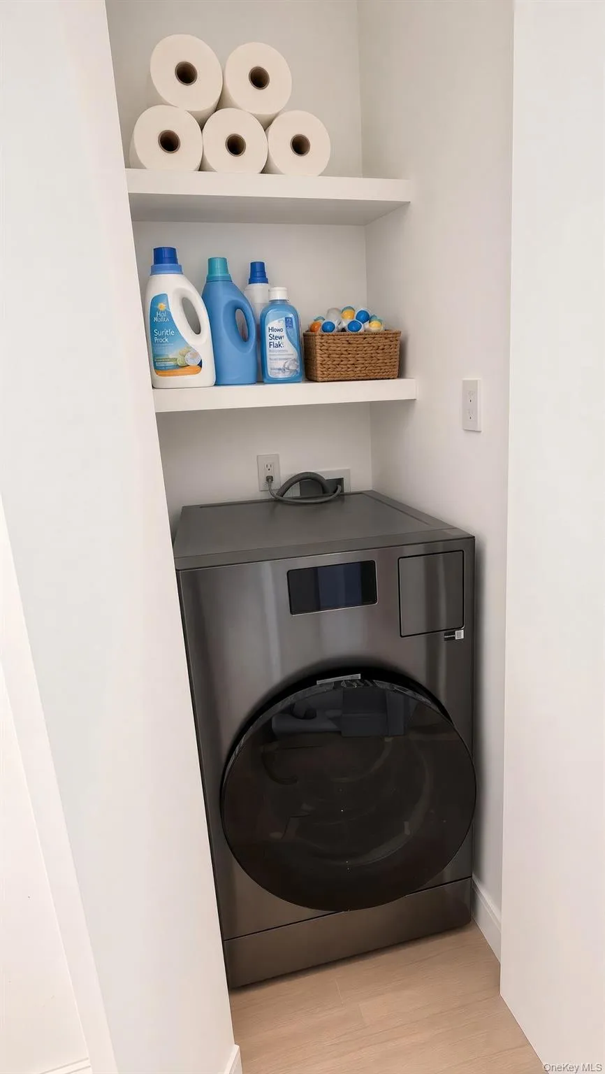 Dedicated laundry area featuring a front-load washing machine/dryer built-in shelving, and light wood-finish flooring Dedicated laundry area featuring a front-load washing machine/dryer built-in shelving, and light wood-finish flooring
