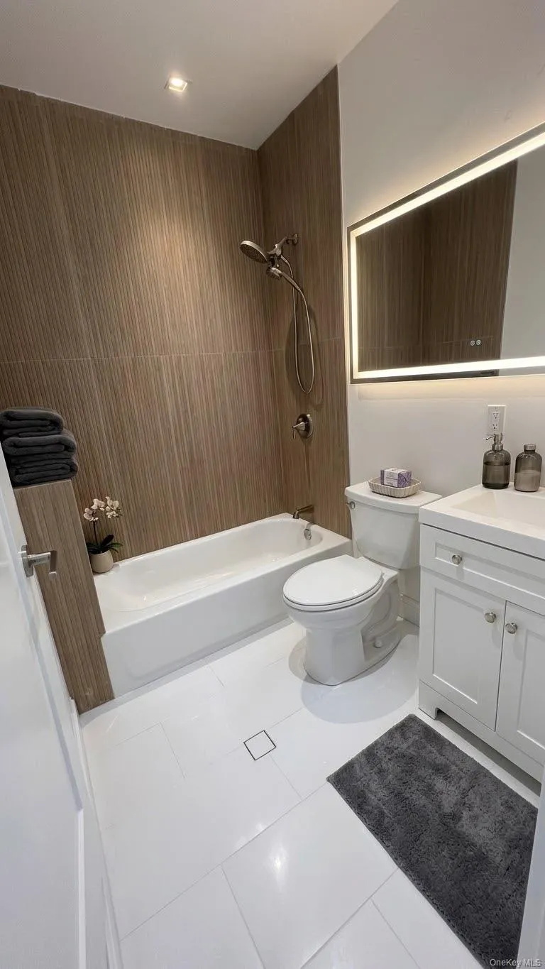 White tile flooring, fluted shower wall tile, a recessed lighting fixture, and a built-in bathtub with a shower fixture. White tile flooring, fluted shower wall tile, a recessed lighting fixture, and a built-in bathtub with a shower fixture.
