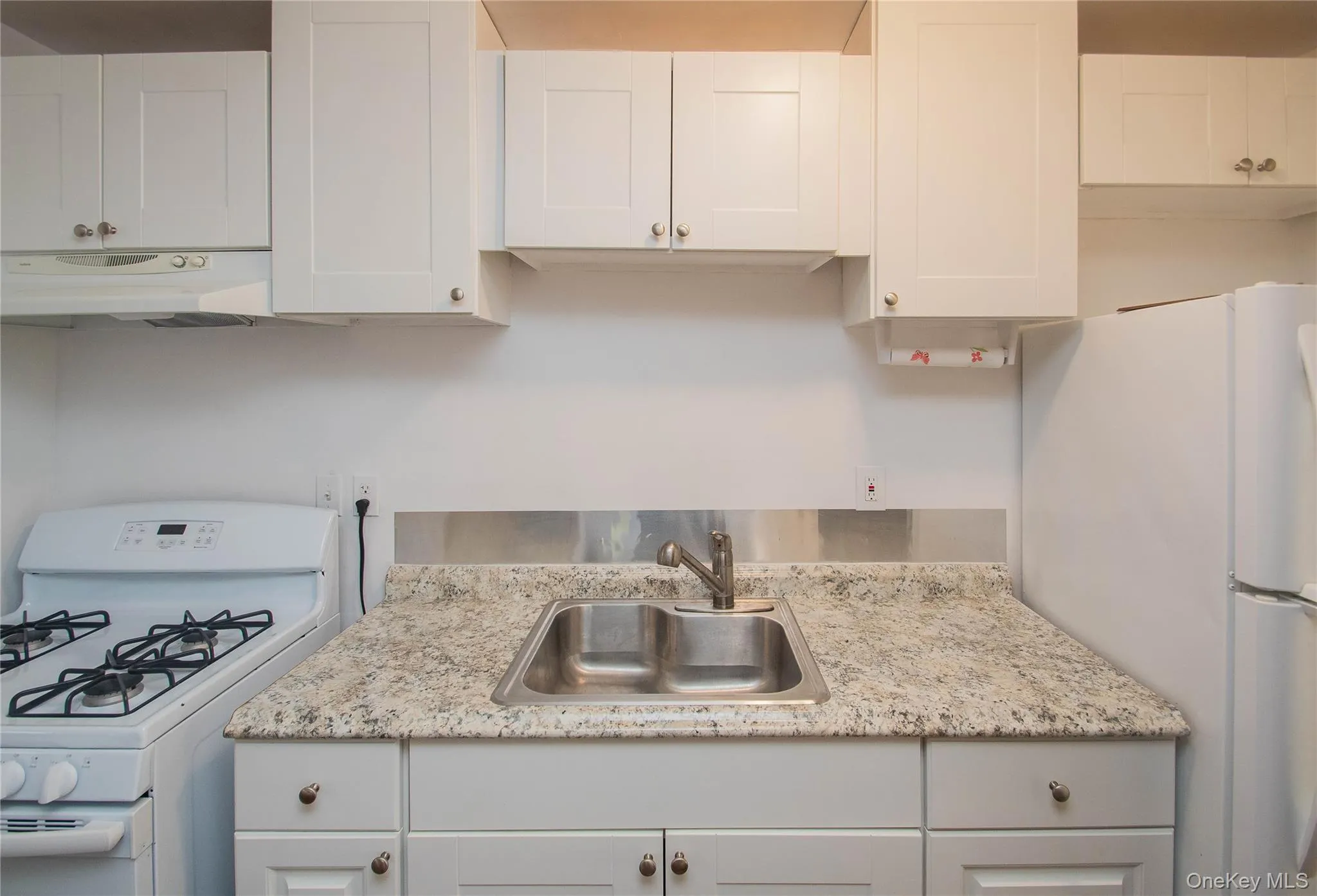 Kitchen with white appliances, gas stove, white cabinetry, under cabinet range hood, and light stone countertops Kitchen with white appliances, gas stove, white cabinetry, under cabinet range hood, and light stone countertops