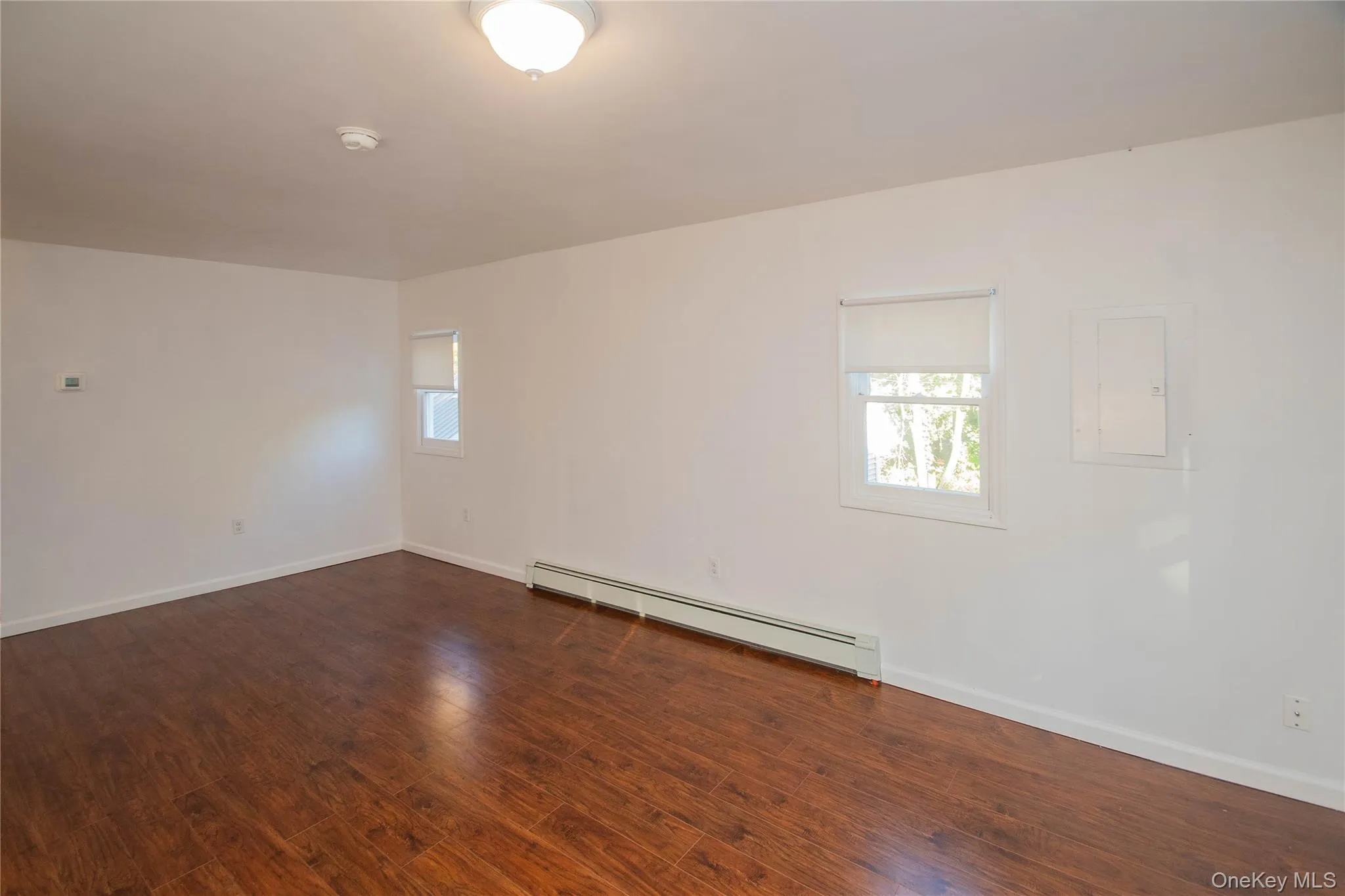 Living room area from entry way, baseboard heating unit, dark wood-style floors, smoke detector, and electric panel Living room area from entry way, baseboard heating unit, dark wood-style floors, smoke detector, and electric panel